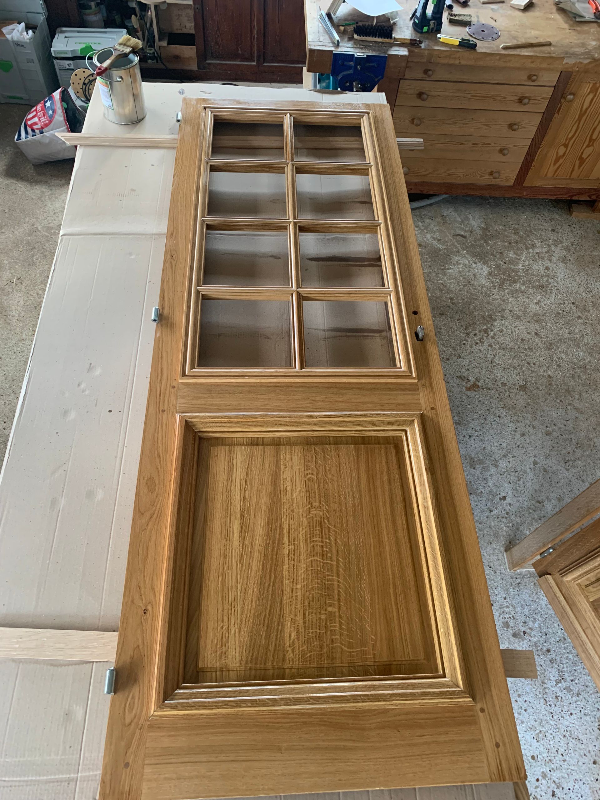 Porte d’armoire en bois avec partie supérieure vitrée et panneau inférieur en relief, posée sur un établi.