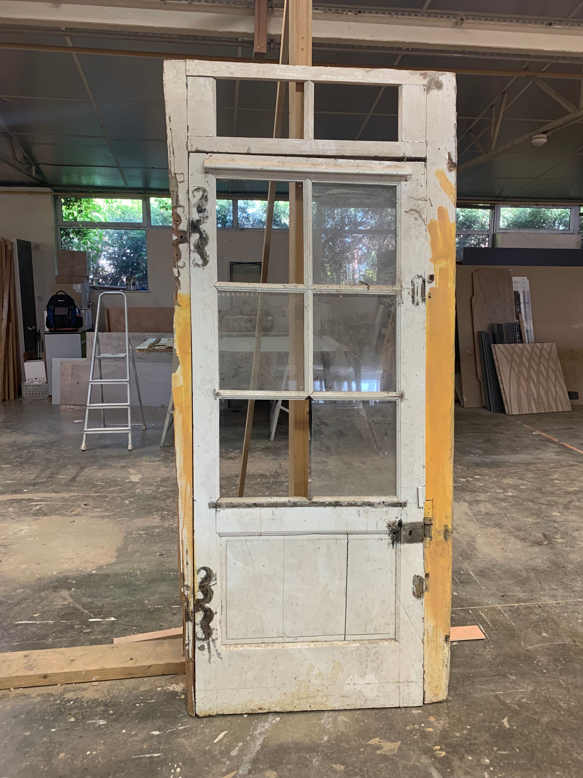 Vieille porte blanche à panneaux vitrés, adossée dans un atelier ou un entrepôt poussiéreux.