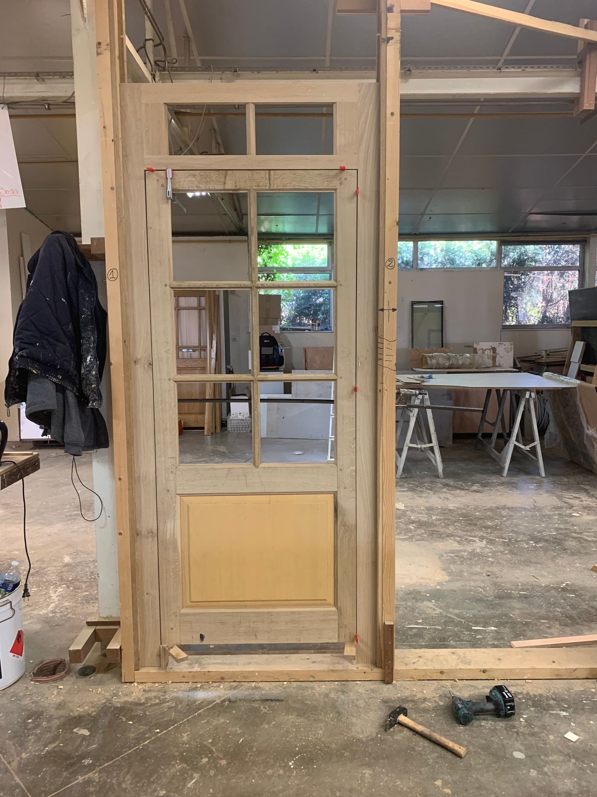 Encadrement en bois partiellement installé dans l’embrasure d’une porte, au milieu d’un atelier encombré ou d’un chantier de rénovation en intérieur.