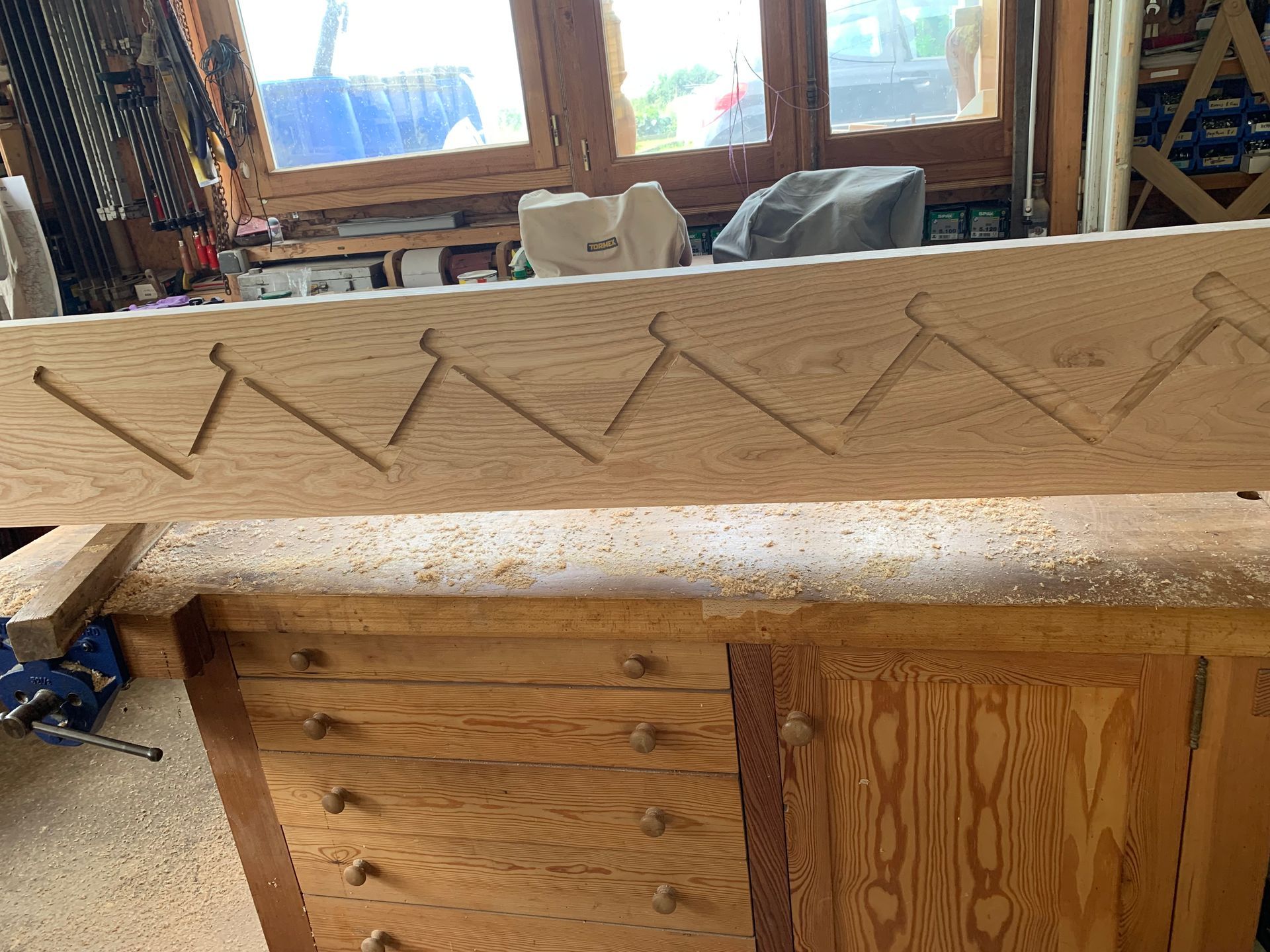 Banc en bois avec des ornements en zigzag sculptés dans un atelier, avec des fenêtres et des outils en arrière-plan.