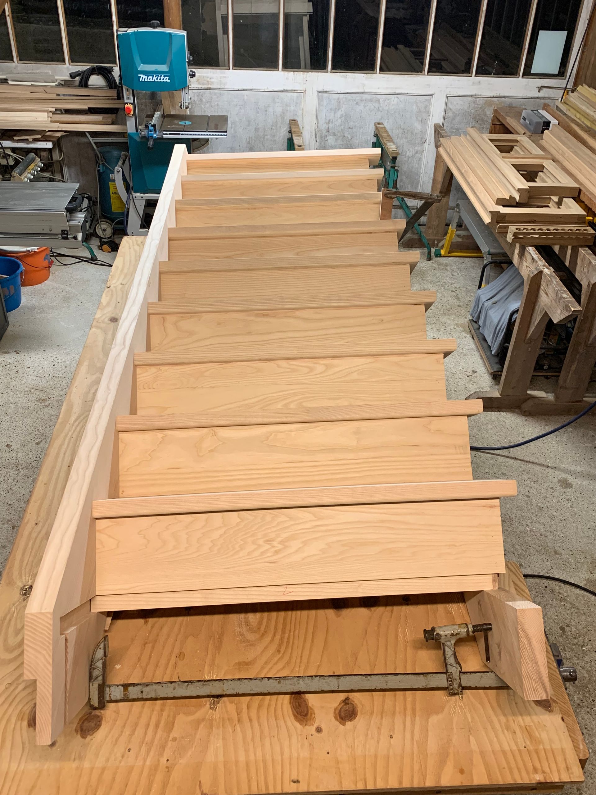 Marches d’escalier en bois dans un atelier, avec des planches brutes et des serre-joints sur un établi.