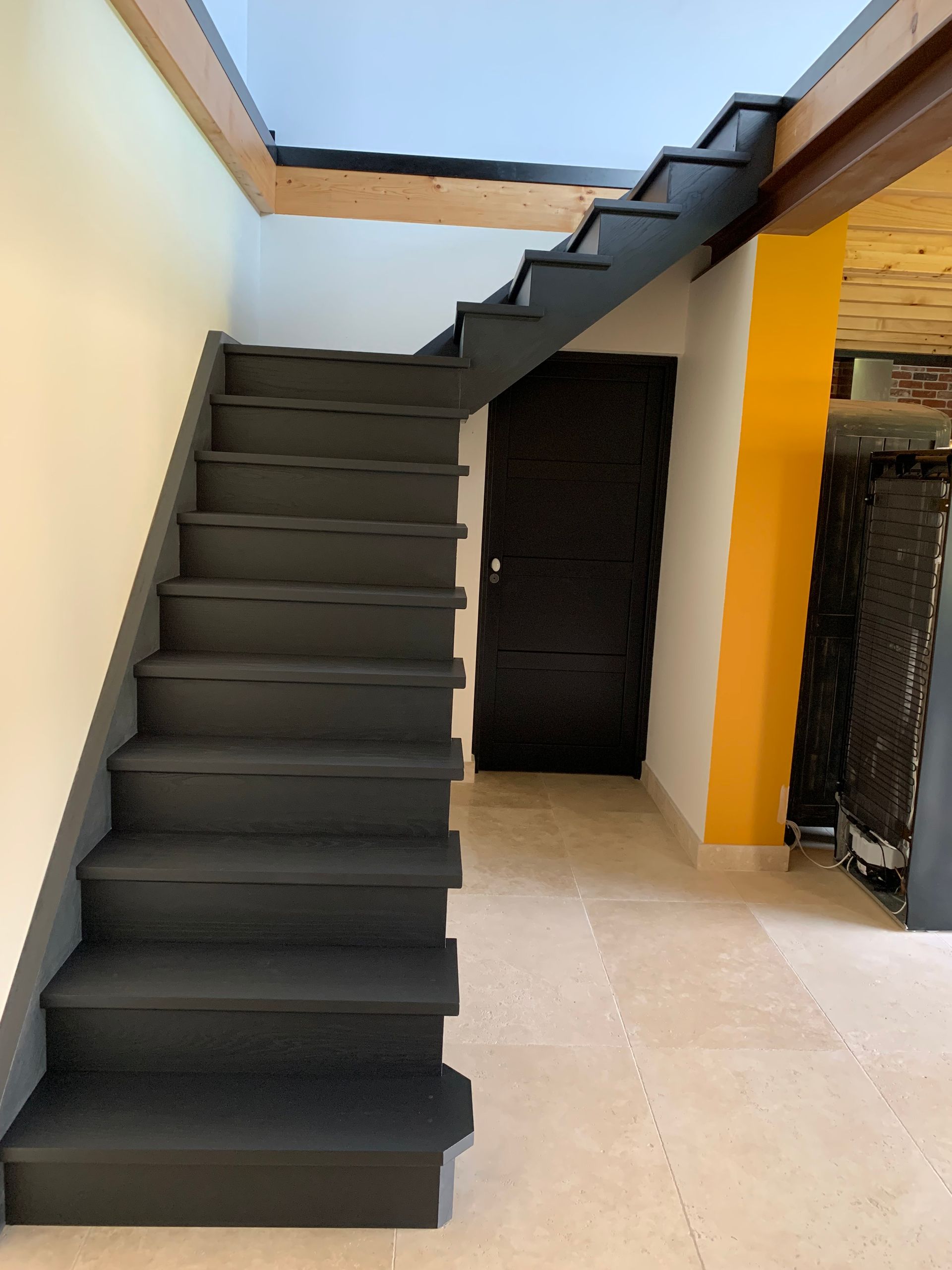 Escalier intérieur avec des marches sombres et une rampe noire dans un couloir lumineux.