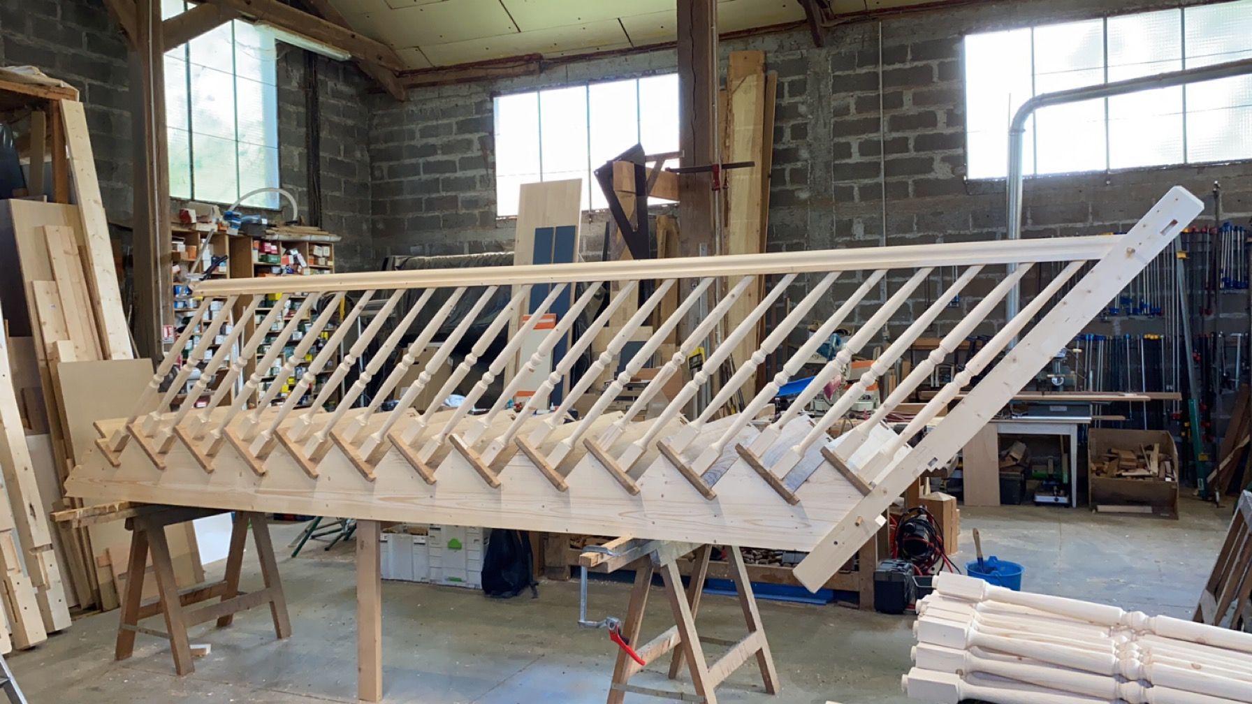 Escalier en bois en cours de construction dans un atelier, avec des membrures et des outils éparpillés.