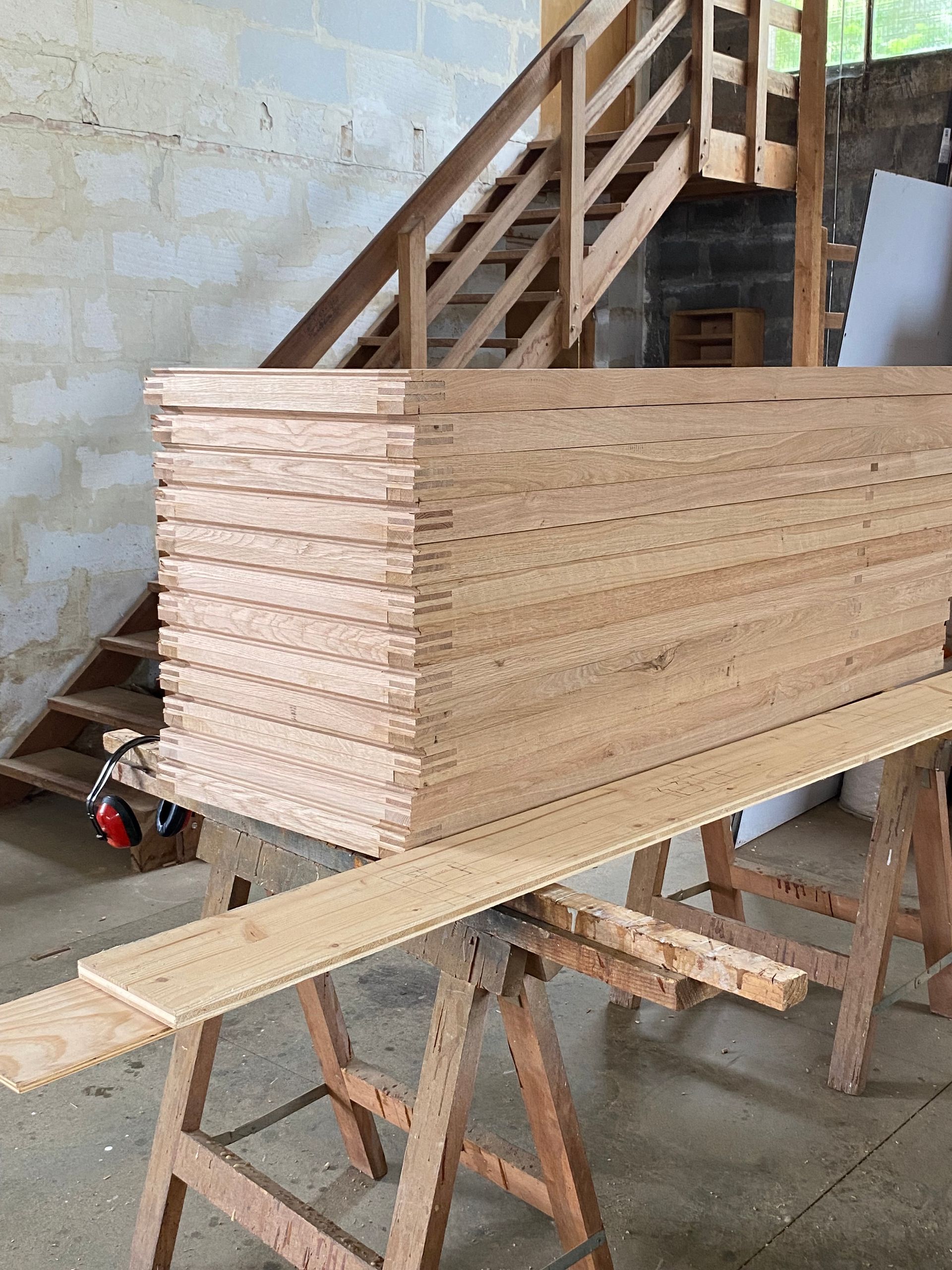 Des planches de bois empilées sur un tréteau d’atelier, à côté d’un escalier dans une pièce en travaux