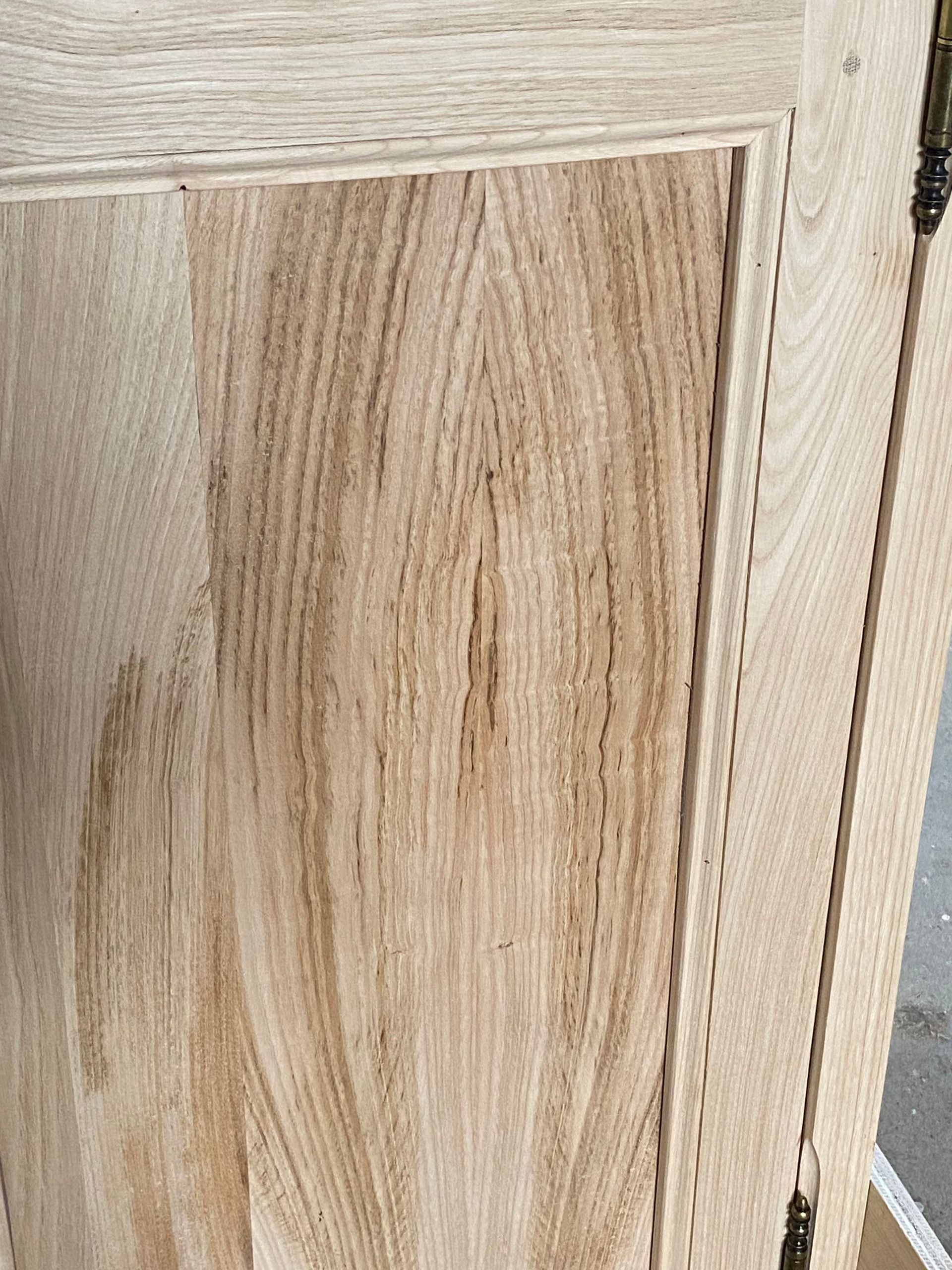 Gros plan sur une porte d’armoire en bois clair, ornée d’un panneau rectangulaire en relief et au grain visible.