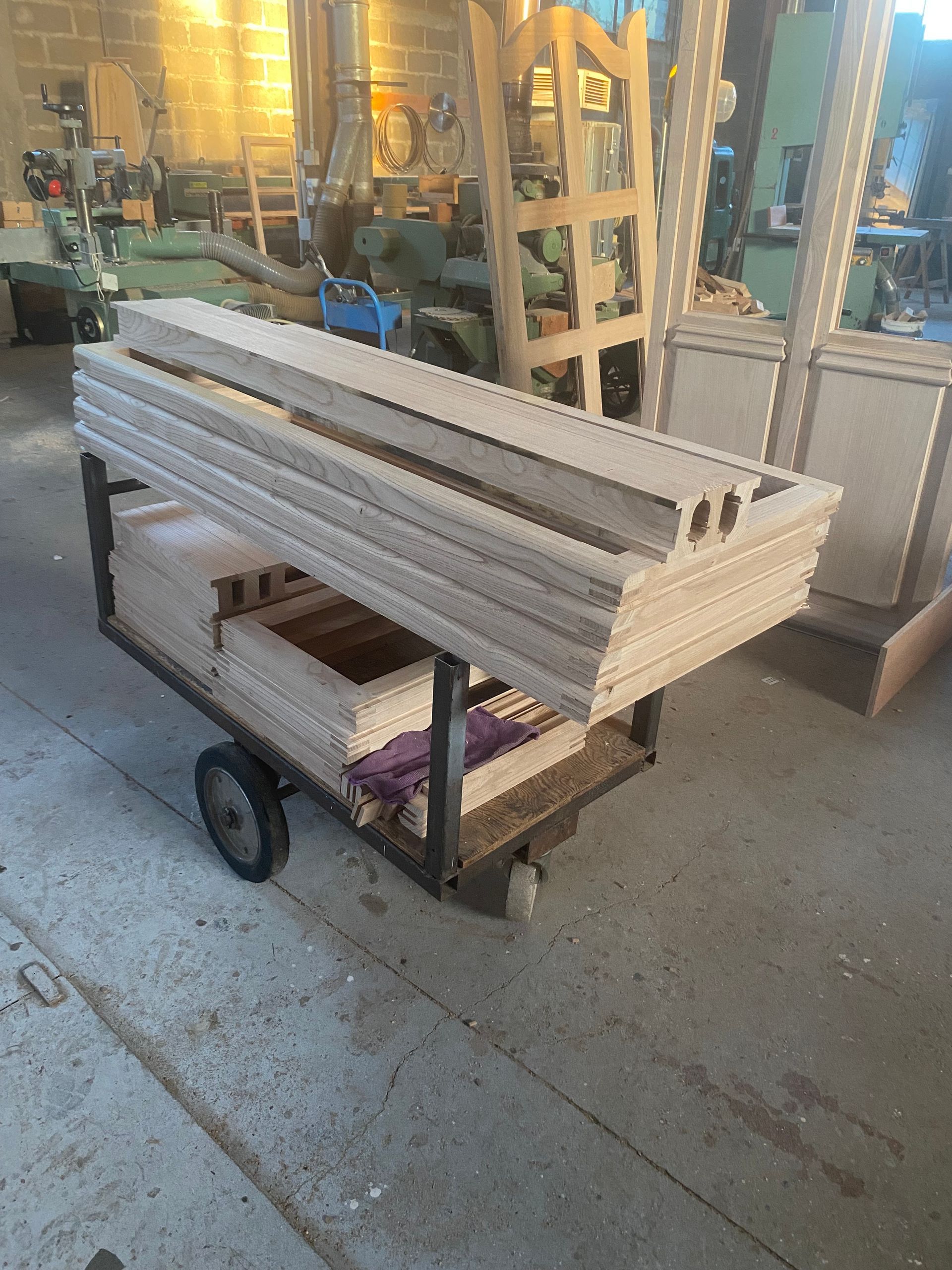 Longues planches blanches empilées sur un chariot à roulettes dans l’allée d’un atelier ou d’un entrepôt.
