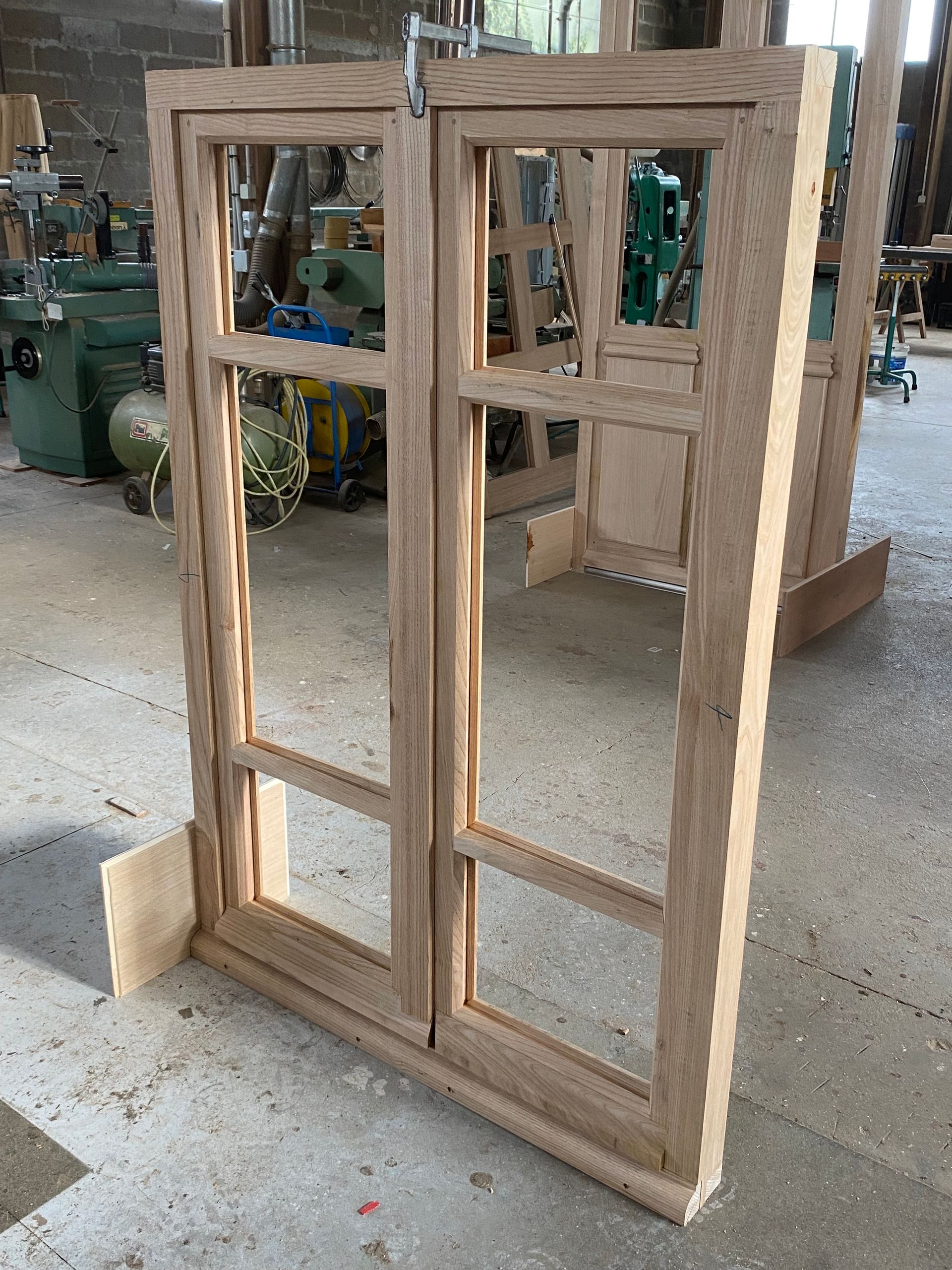 Cadre de fenêtre en bois inachevé, debout dans un atelier, sans ses vitres.
