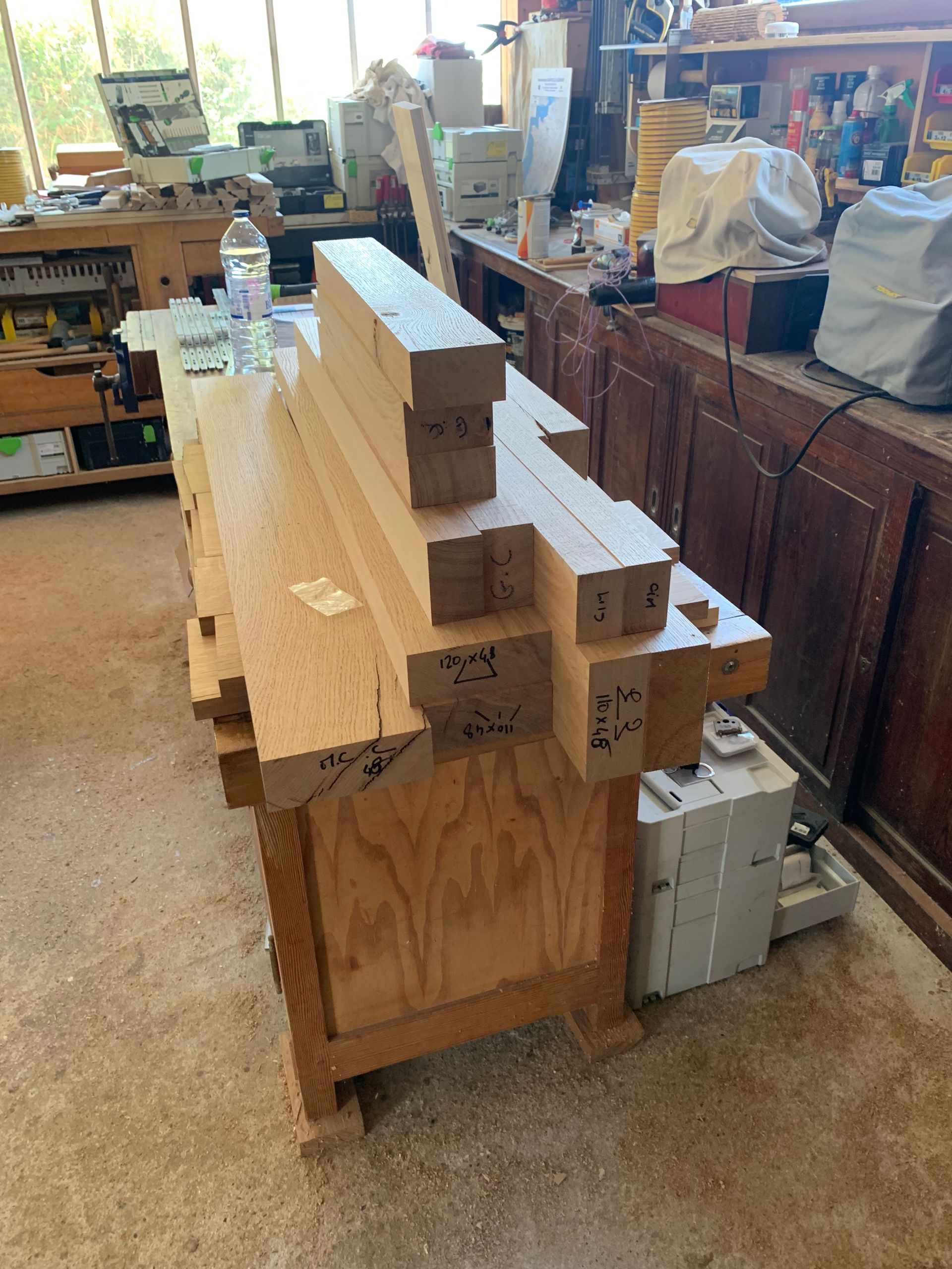 Planches de bois empilées et blocs de bois sur un chariot dans un atelier, avec des outils et du matériel en arrière-plan.