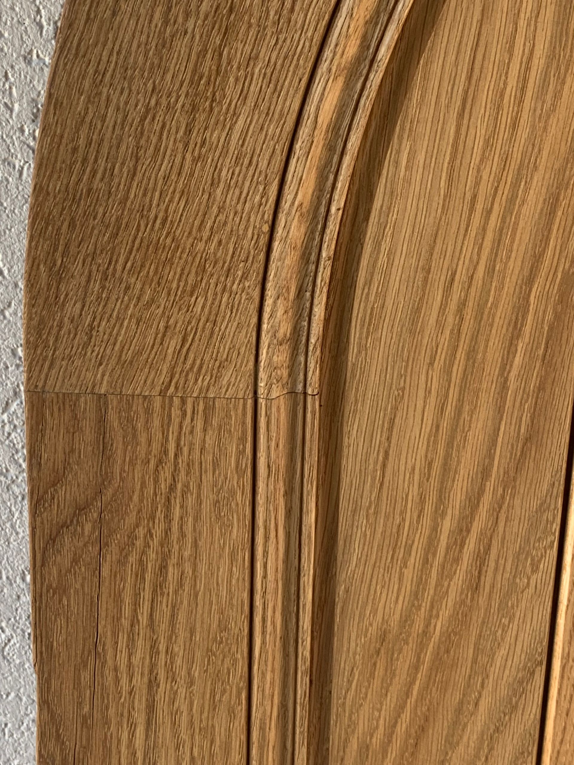 Gros plan sur le veinage courbe du bois, avec une ligne de joint et un fond beige texturé.