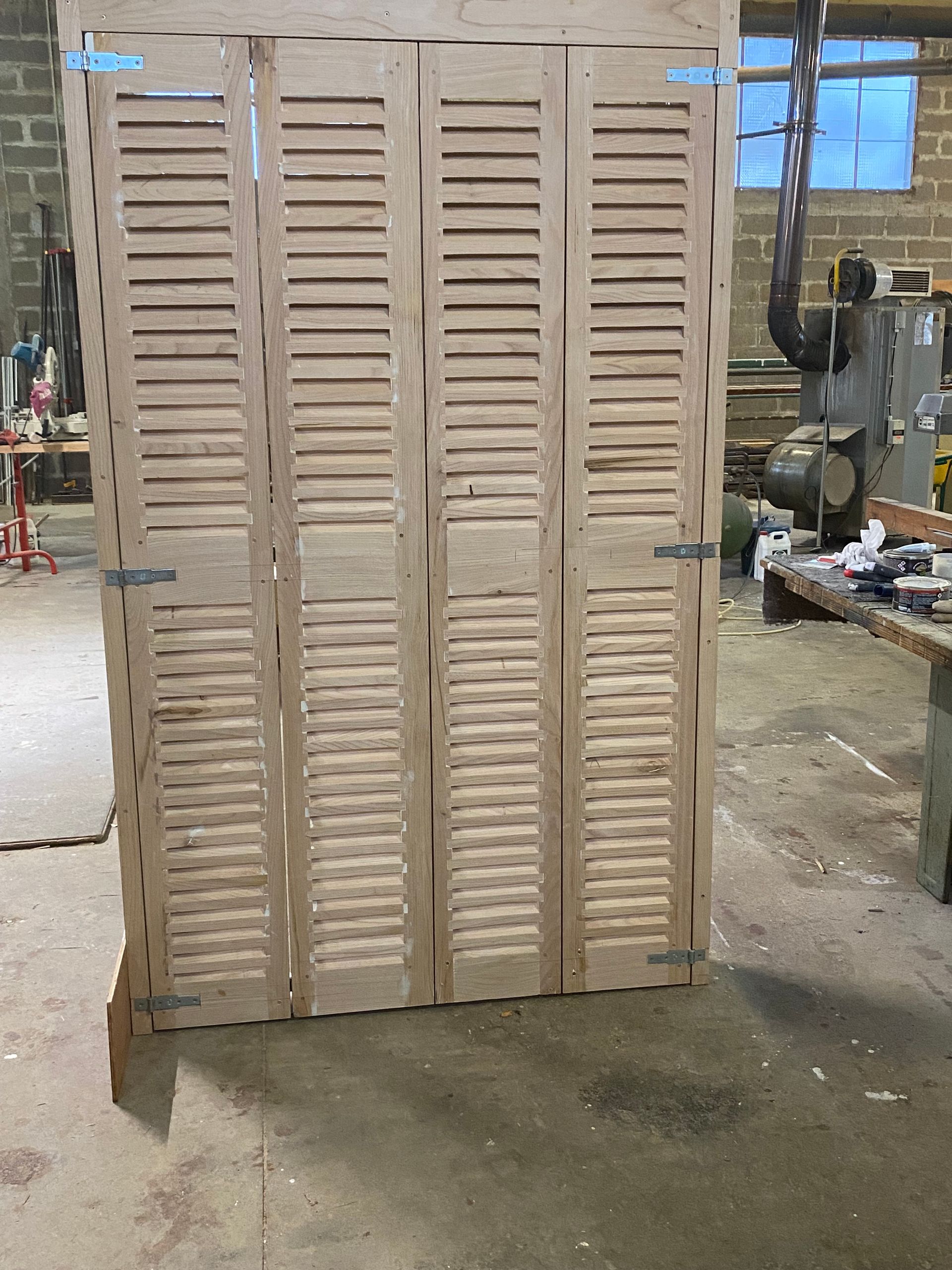 Paravent pliant en bois beige à panneaux à persiennes, installé dans un atelier.