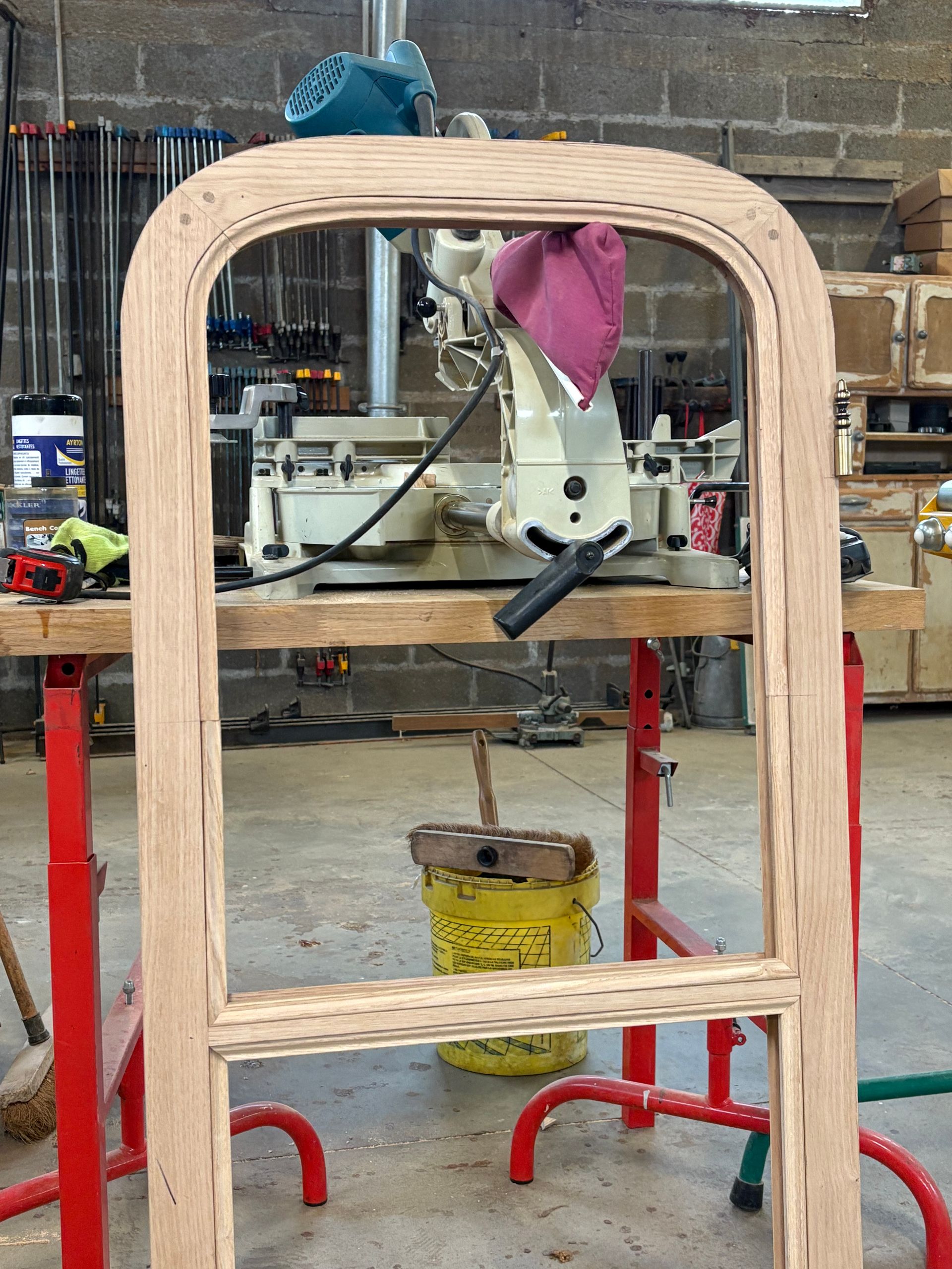 Cadre de fenêtre en bois dans un atelier, avec un bras robotisé et des outils visibles derrière.