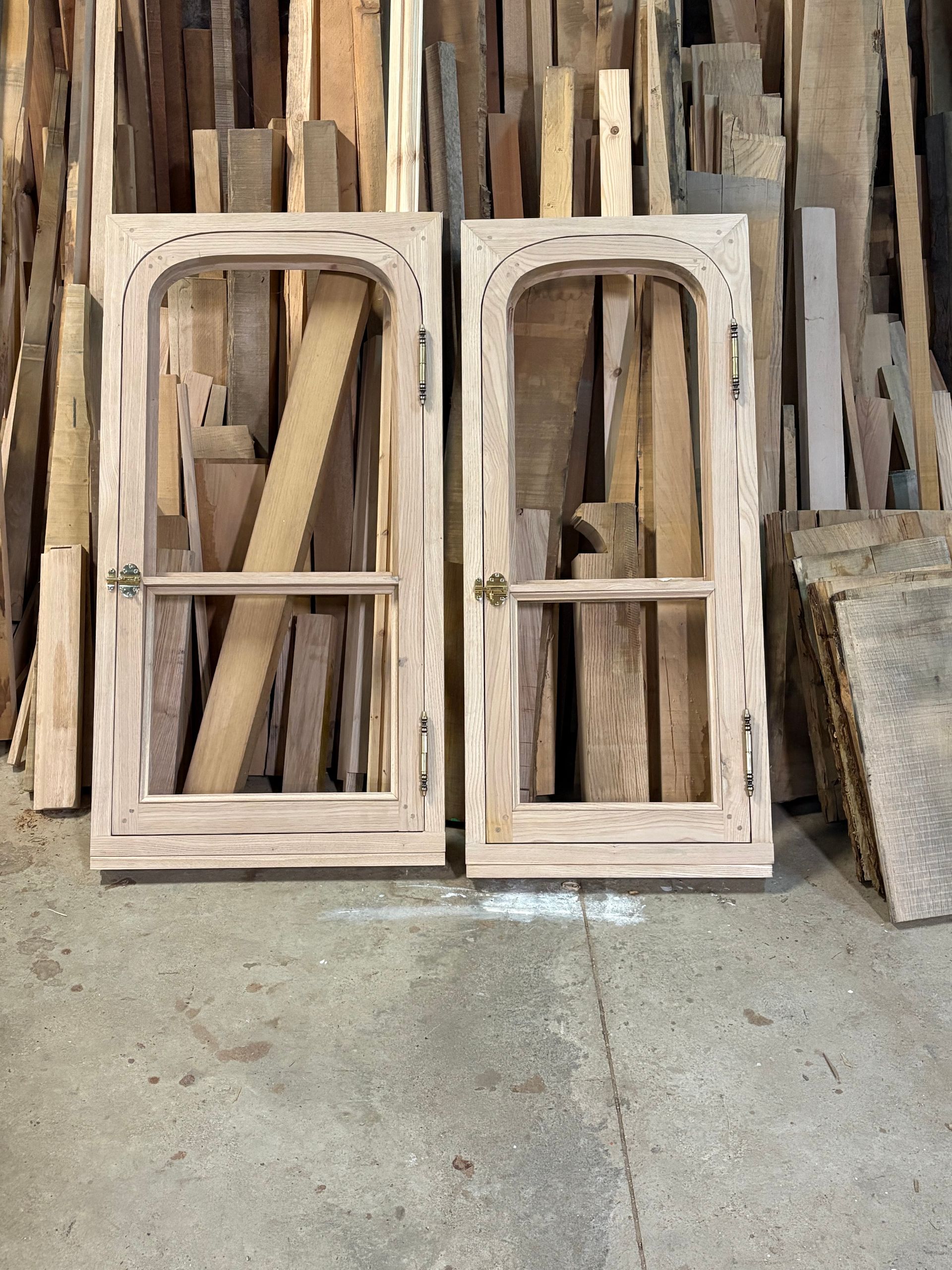 Deux cadres de fenêtre en bois appuyés contre des planches empilées dans un atelier ou une scierie.