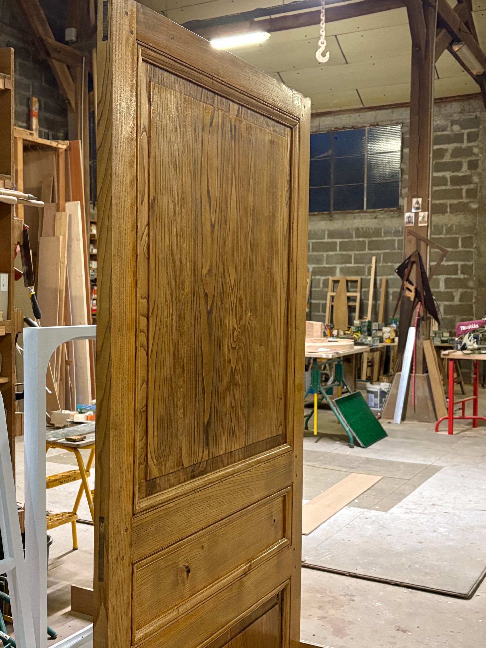 Armoire haute en bois ou panneau de porte dans un atelier, avec des outils et du matériel en arrière-plan.