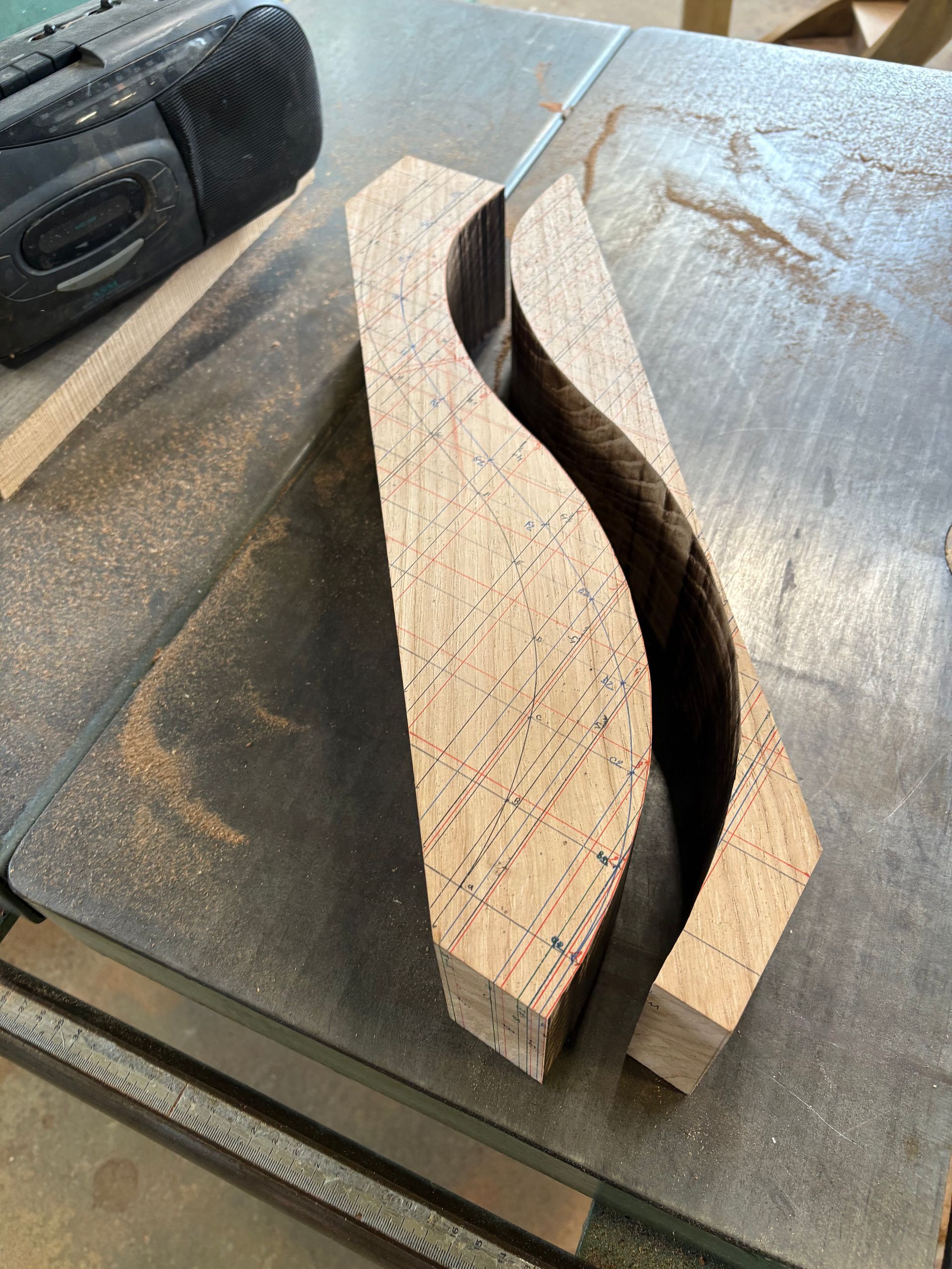 Deux pièces de bois incurvées sur une table d’atelier, avec un outil plus sombre en arrière-plan.