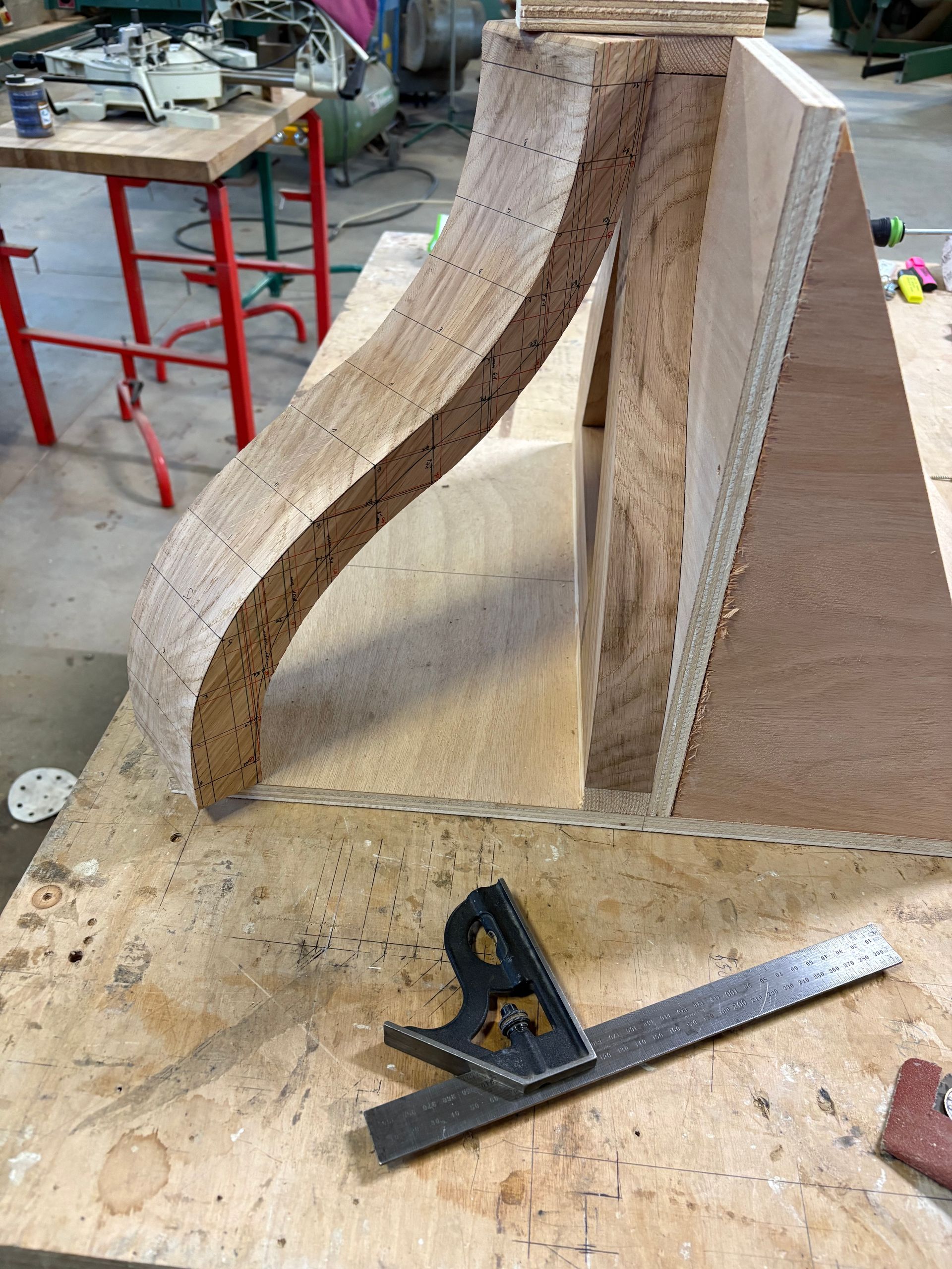 Gabarit d’atelier avec des pièces de bois courbées sur un établi, entouré d’outils et de sciure.