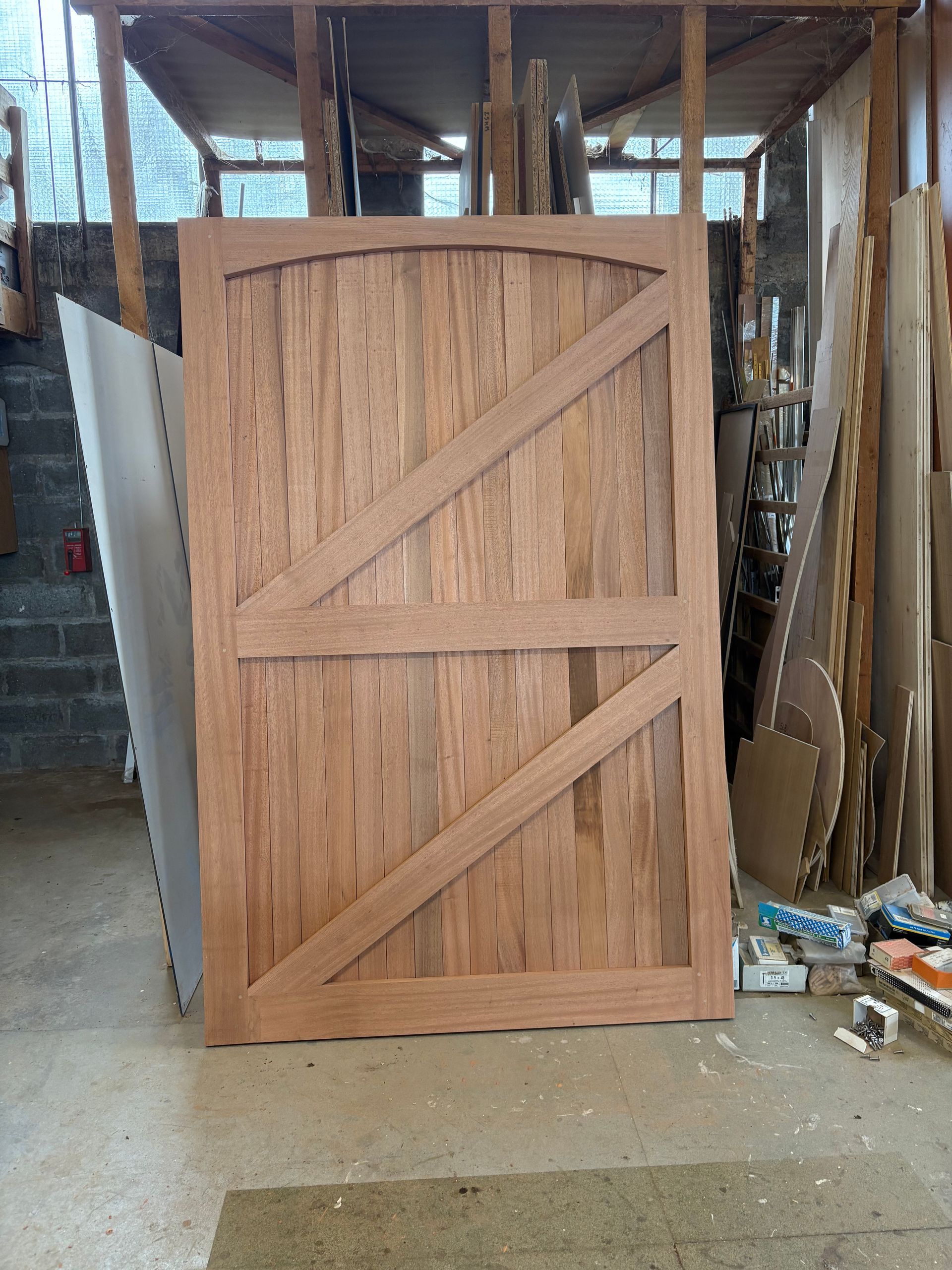 Porte de caisse en bois posée à la verticale dans un atelier, avec des renforts diagonaux et des outils à proximité.