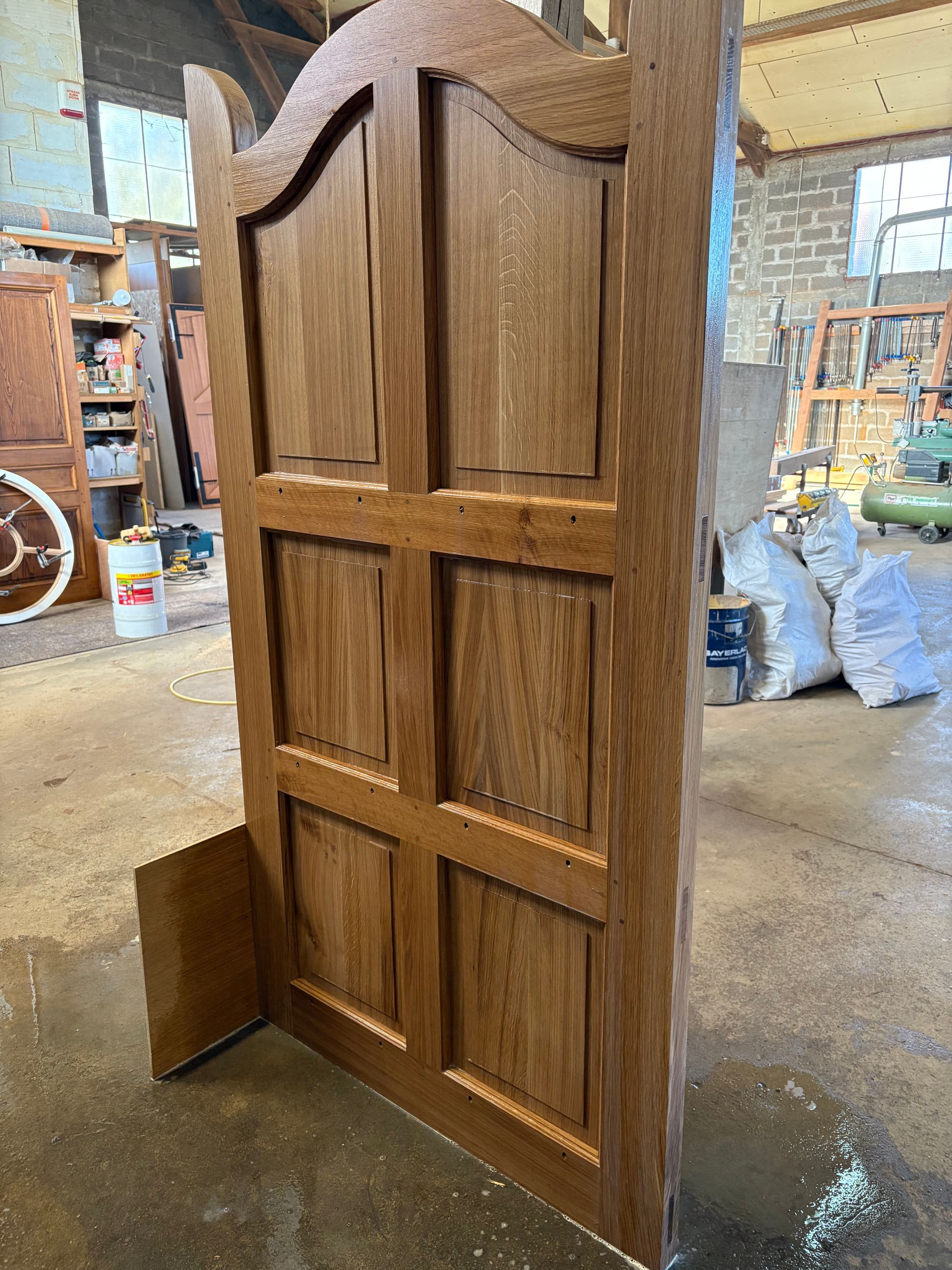 Porte en bois dans un atelier, avec un sommet en arc et une finition en bois foncé.