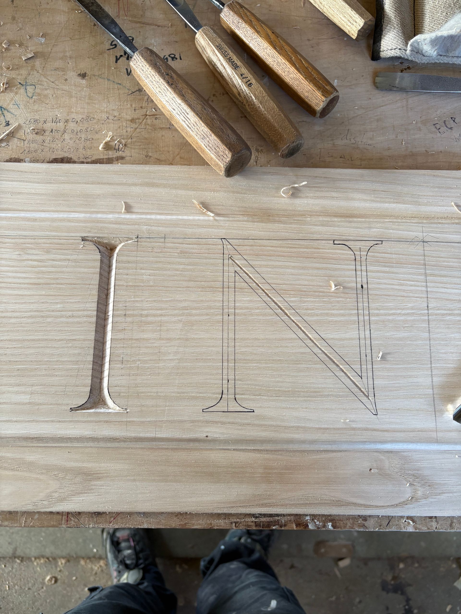 Planche en bois gravée des lettres I, T et N, avec des ciseaux posés au-dessus sur un établi.