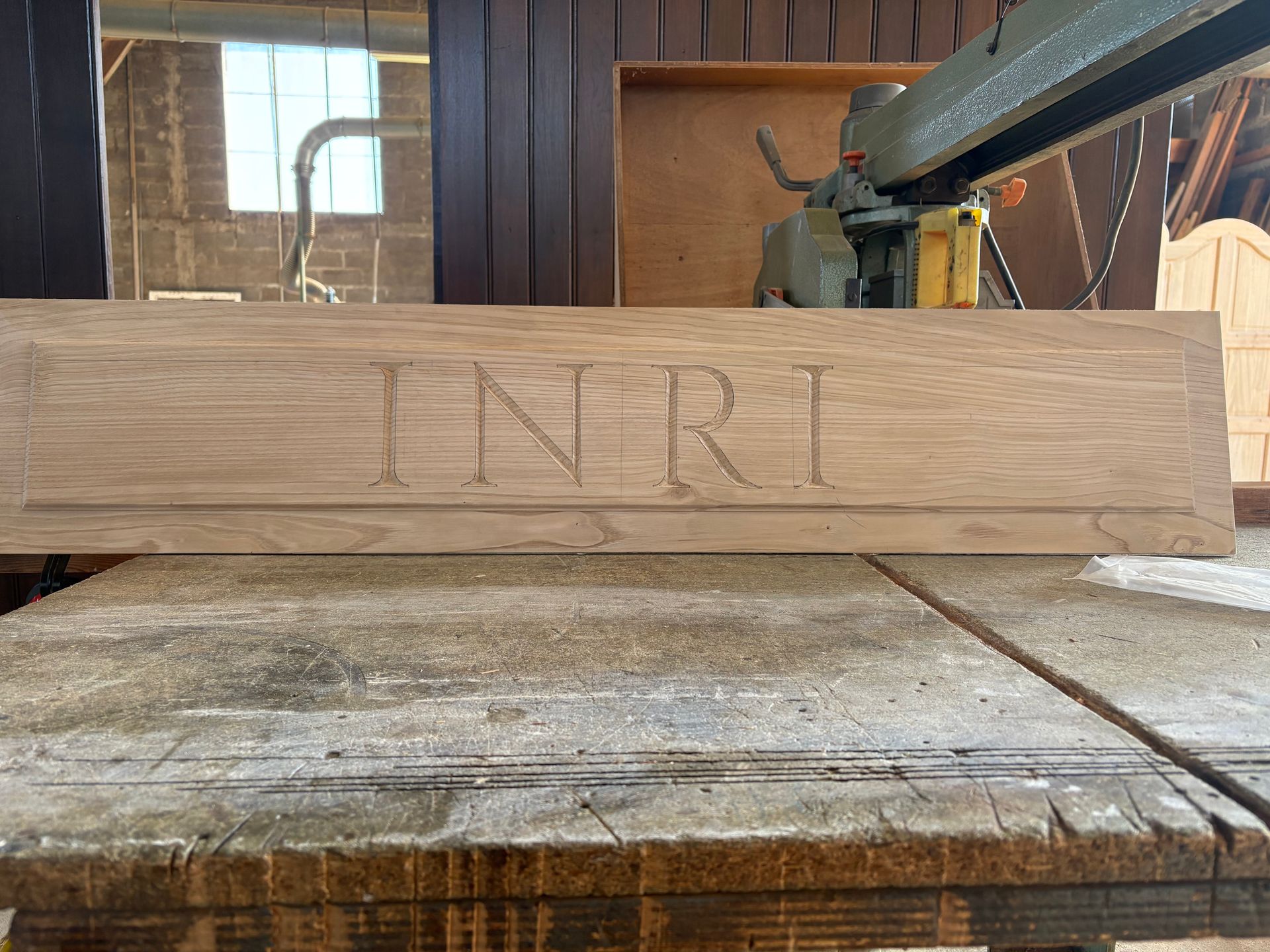 Enseigne en bois avec les lettres gravées, posée sur un établi usé dans un atelier.