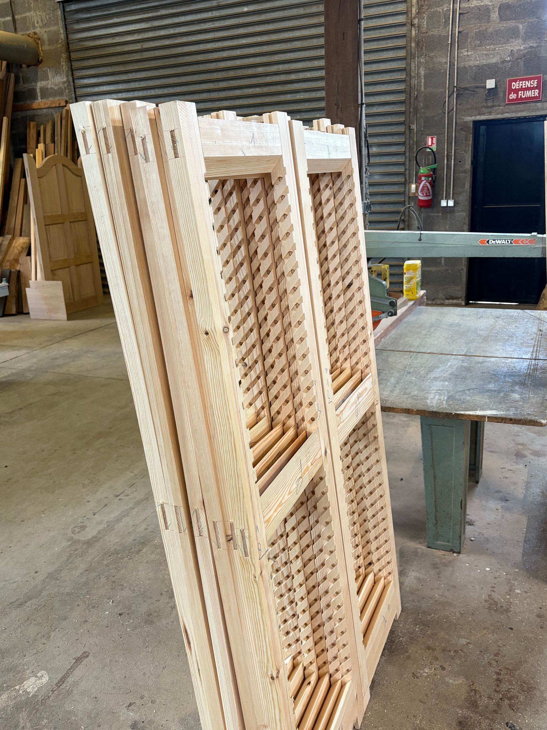 Des palettes en bois empilées dans un entrepôt industriel, près d’une table métallique et d’un quai de chargement.