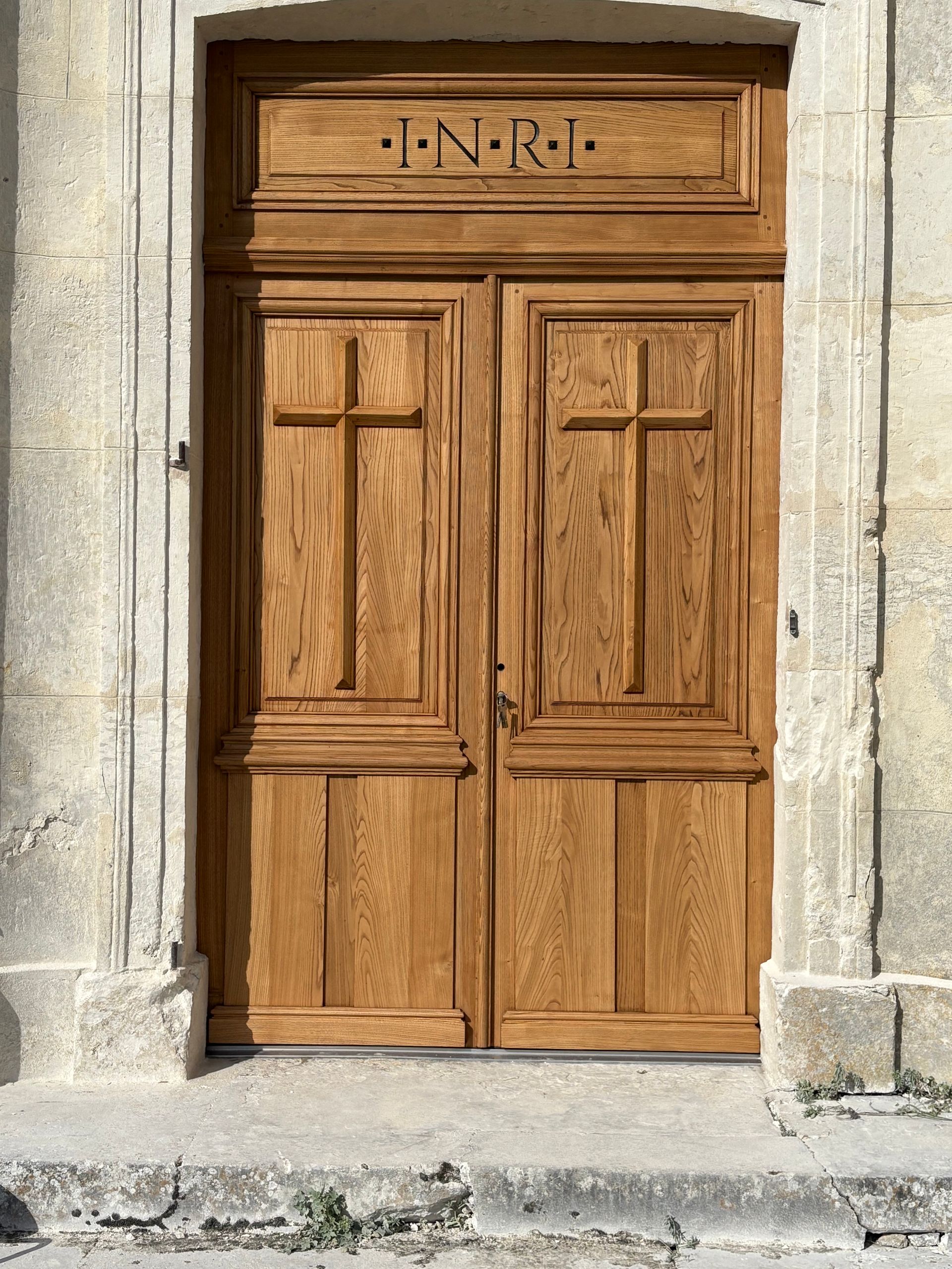 Ensemble de doubles portes en bois dans une ouverture en pierre, surmonté d’un panneau sculpté.