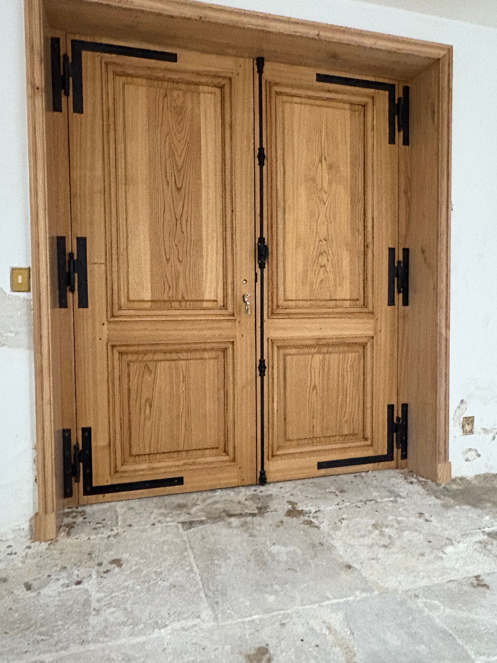 Doubles portes en bois avec des charnières en fer noir, dans l’embrasure intérieure d’une porte en pierre.