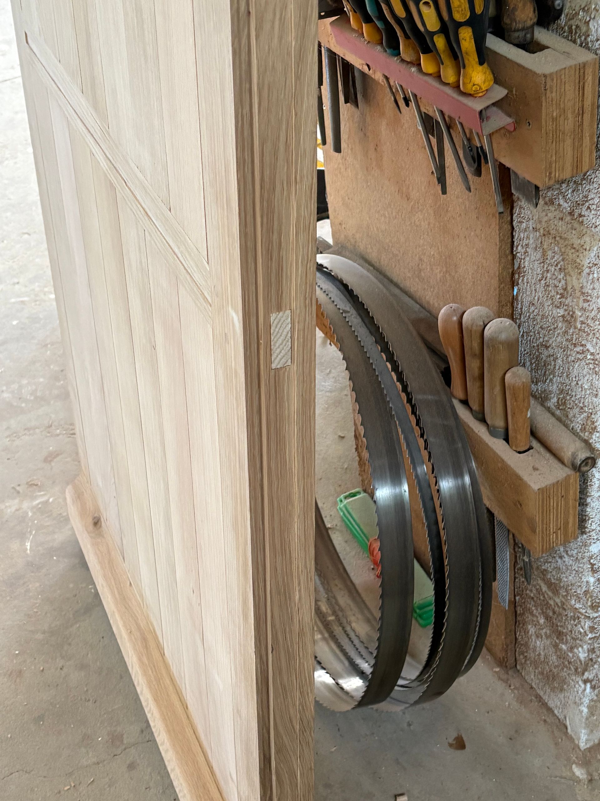 Coin d’atelier avec une grande poulie métallique et des outils accrochés à un panneau mural en bois.