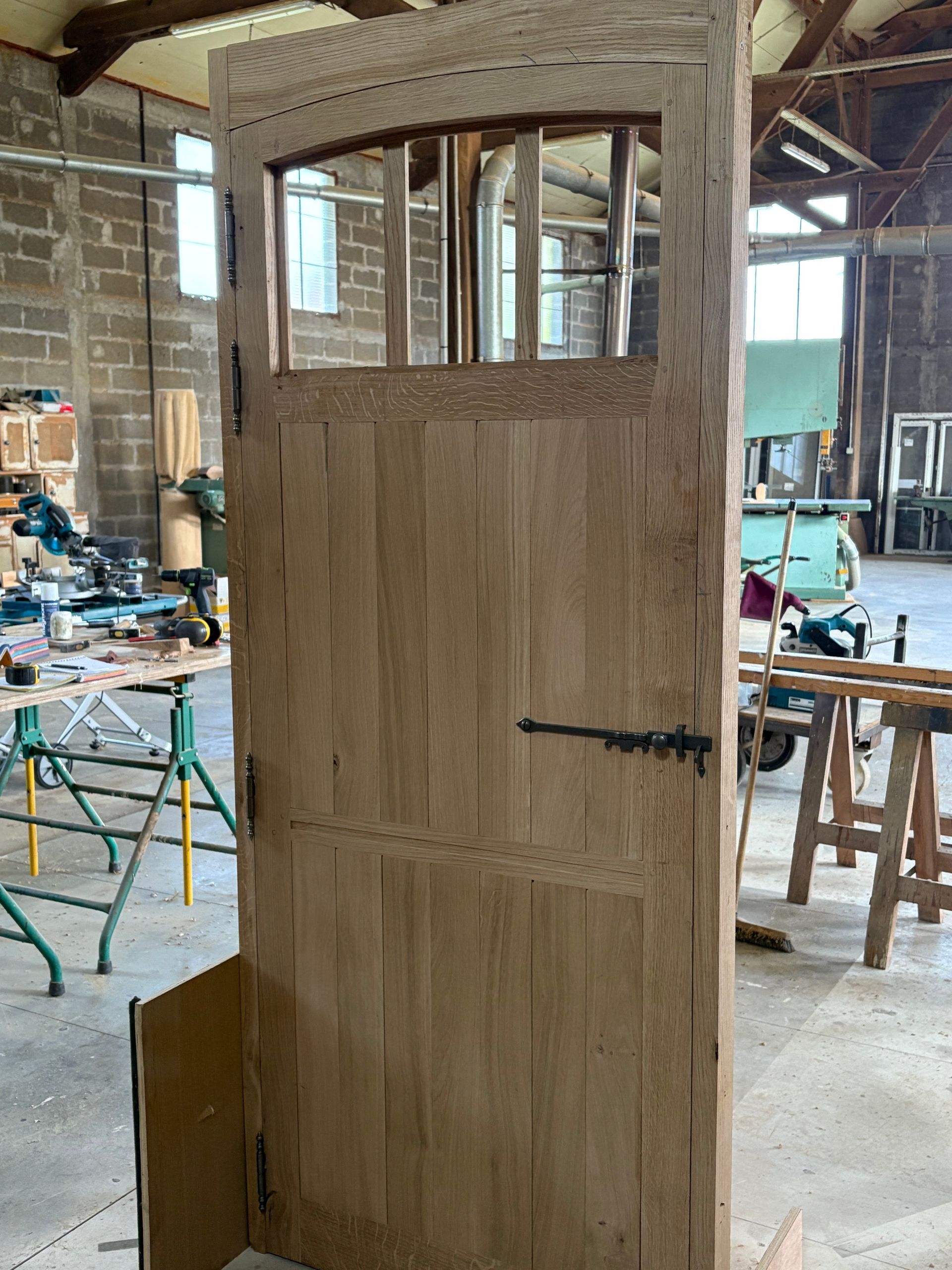 Porte en bois inachevée avec des vitres, dans un atelier, entourée d’outils et de matériaux.