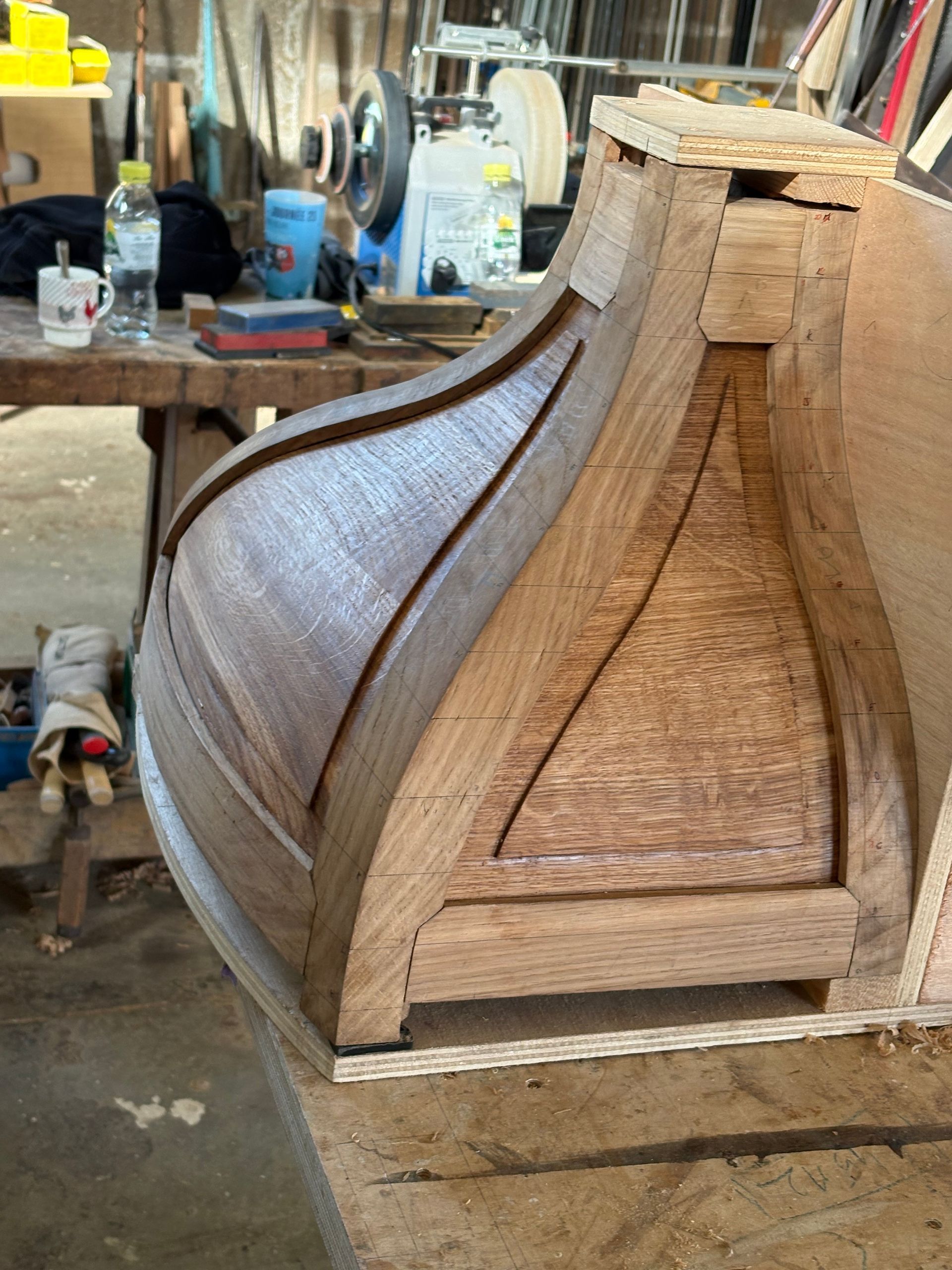 Structure de meuble en bois partiellement tressée dans un atelier, avec des outils et des matériaux en arrière-plan.