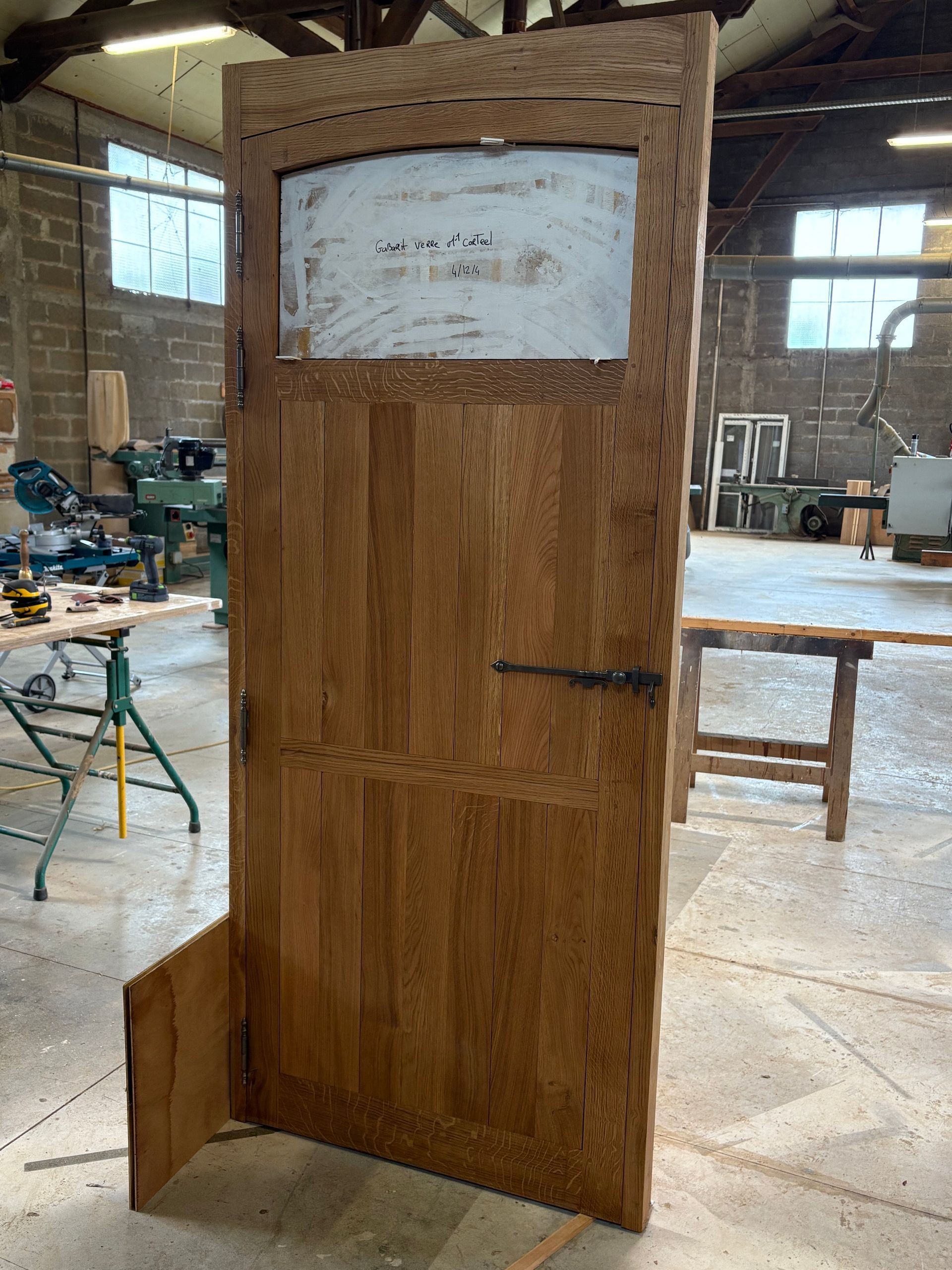 Grand panneau de porte en bois dans un atelier, avec une pancarte blanche fixée près du haut.