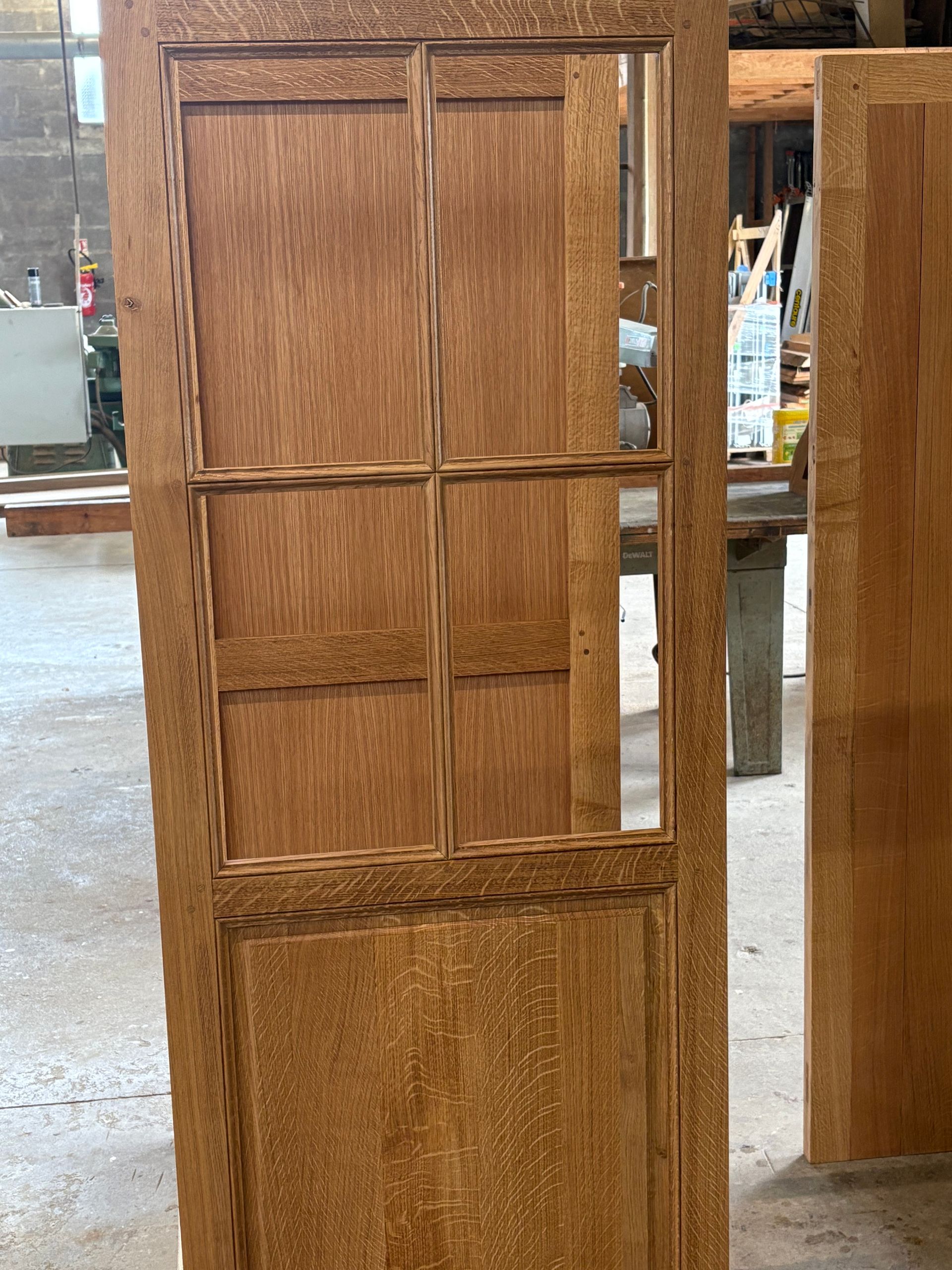 Porte de placard en bois avec des panneaux rectangulaires et des niches à étagères en verre transparent, dans un atelier.