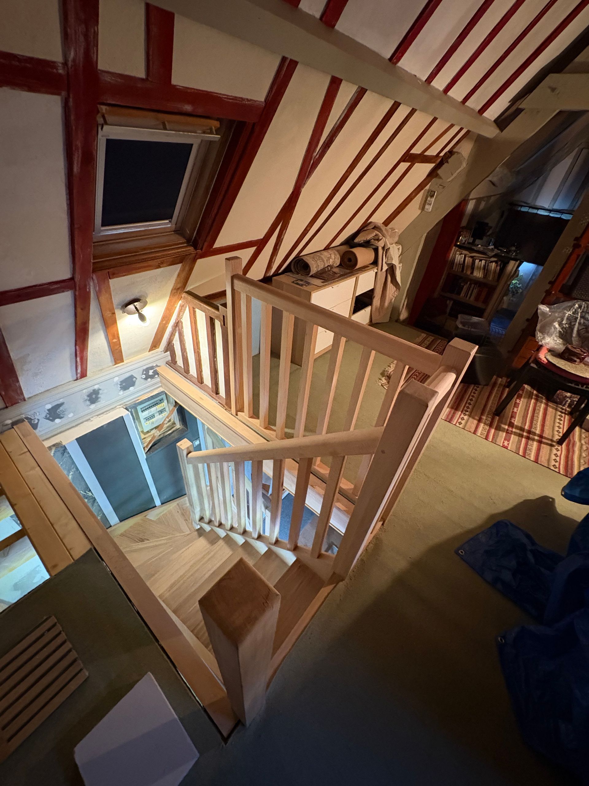 Escalier en bois menant aux combles, avec des marches ouvertes et une rampe, dans un espace intérieur étroit.