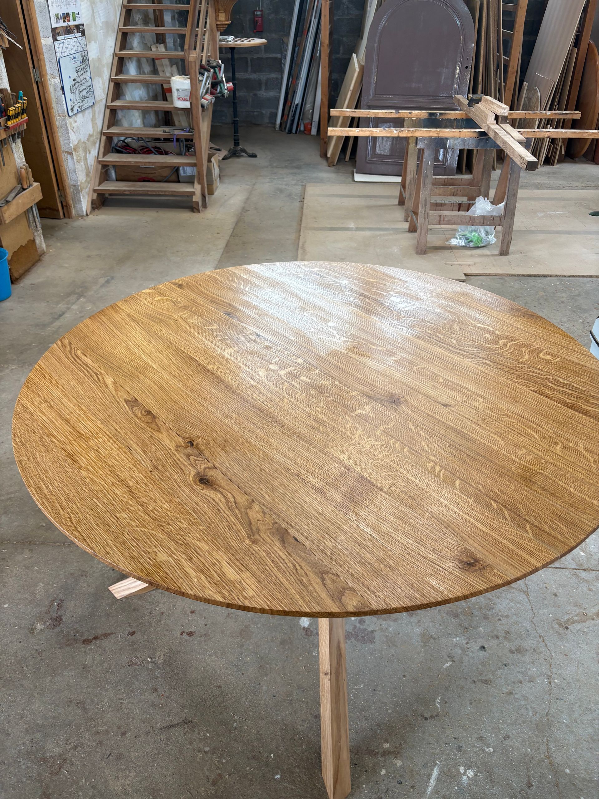 Table ronde en bois tressé, sur un pied central, dans un atelier.