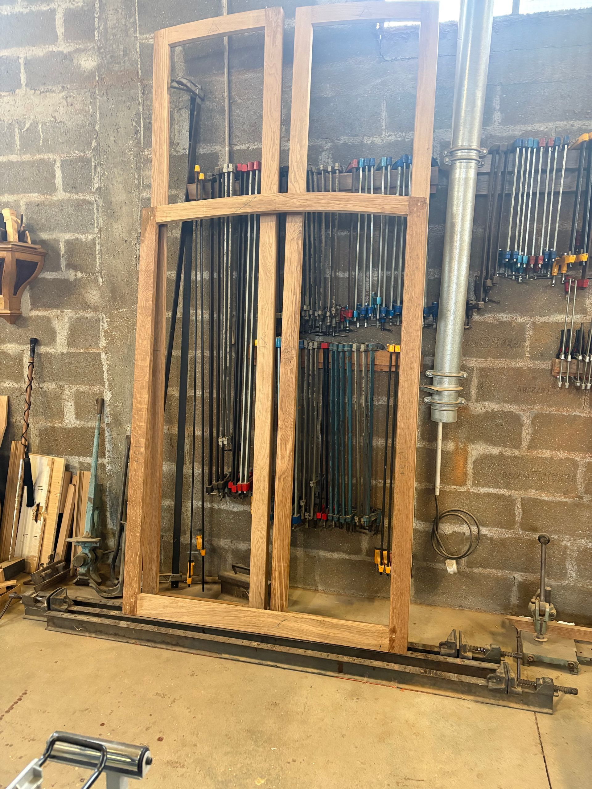Cadre en bois appuyé contre un mur en parpaings dans un atelier, avec des outils et des barres métalliques à proximité.