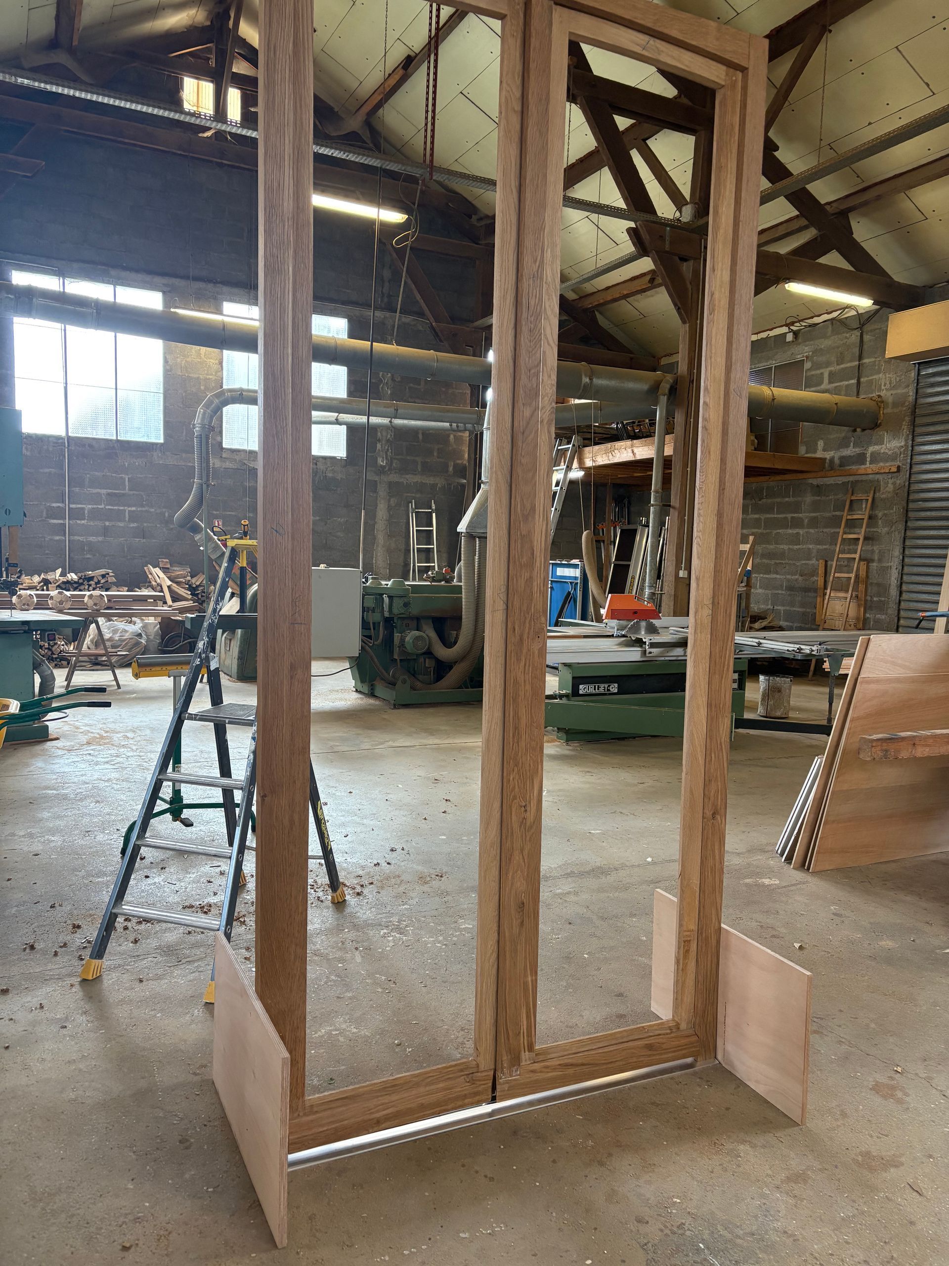 Grand cadre en bois brut avec des panneaux miroir dans un entrepôt industriel.