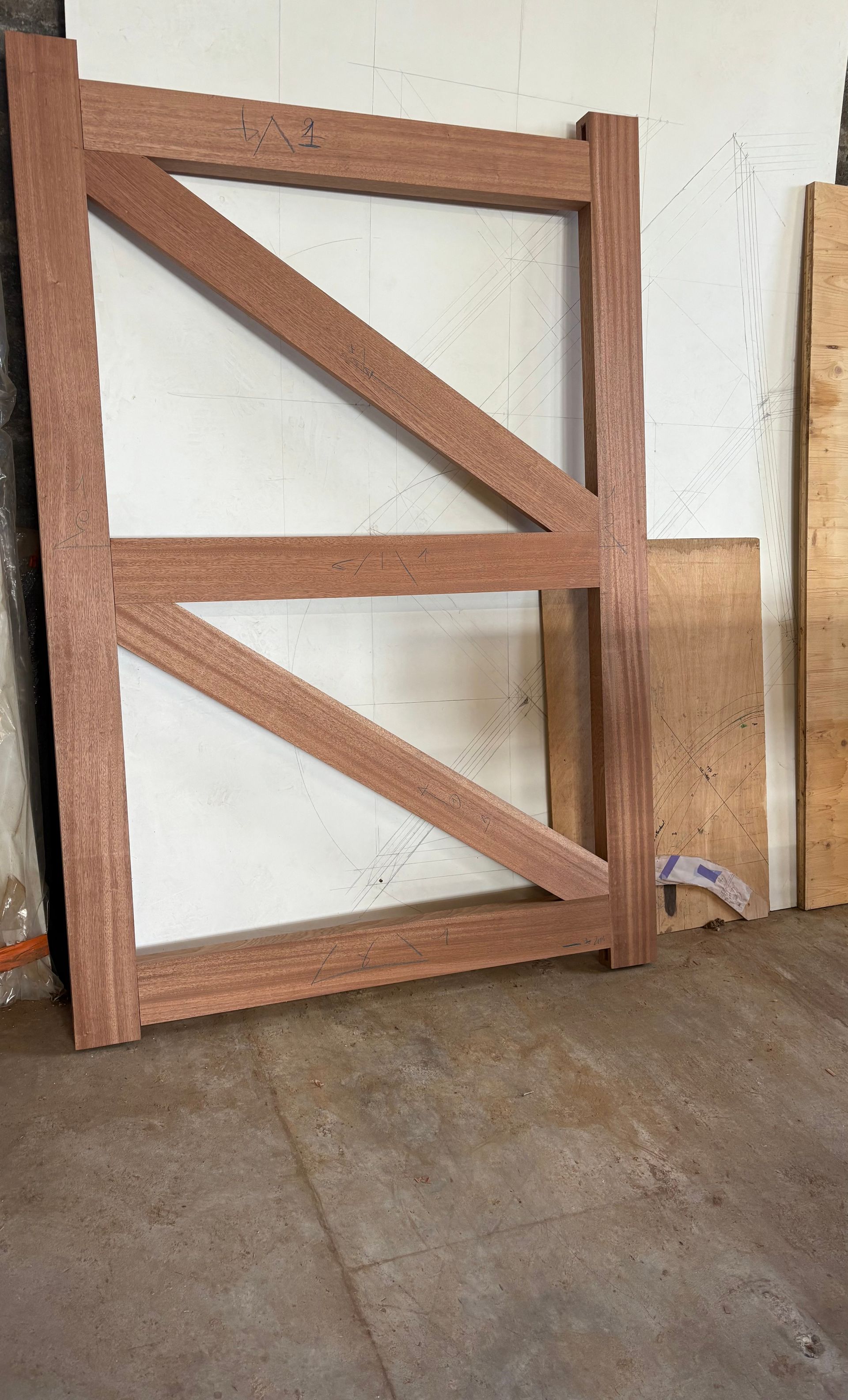 Portail ou panneau de clôture en bois avec des renforts diagonaux, appuyé contre un mur blanc sur un sol en béton.