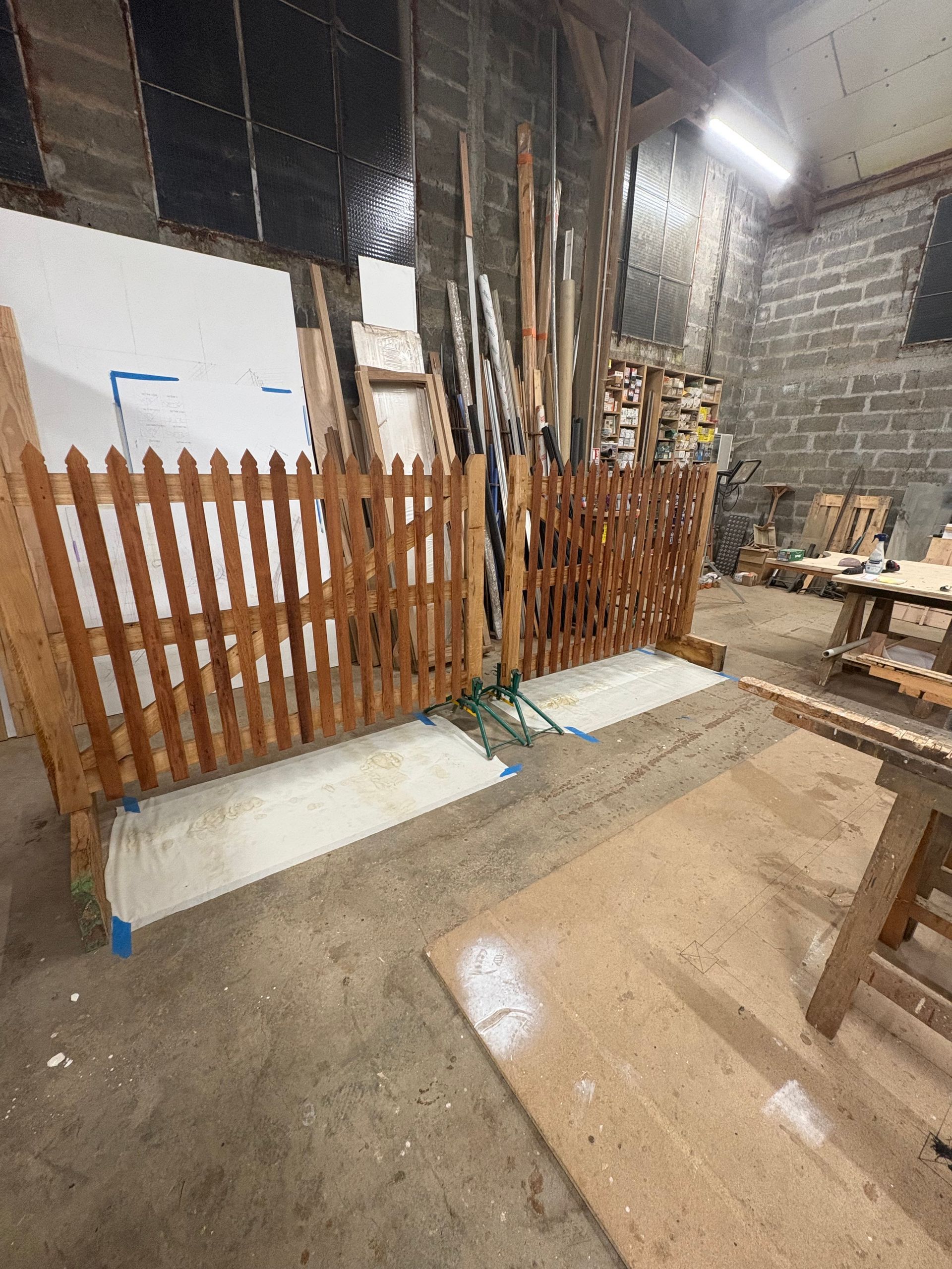 Entrepôt avec une clôture en bois, un sol en béton humide et des matériaux empilés contre des murs en parpaings.