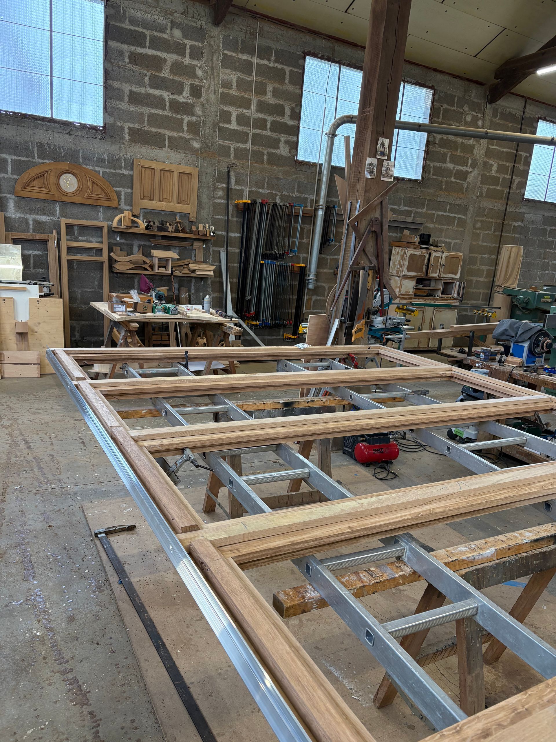 Atelier de menuiserie avec un grand cadre en bois en cours de fabrication, posé sur des tréteaux.