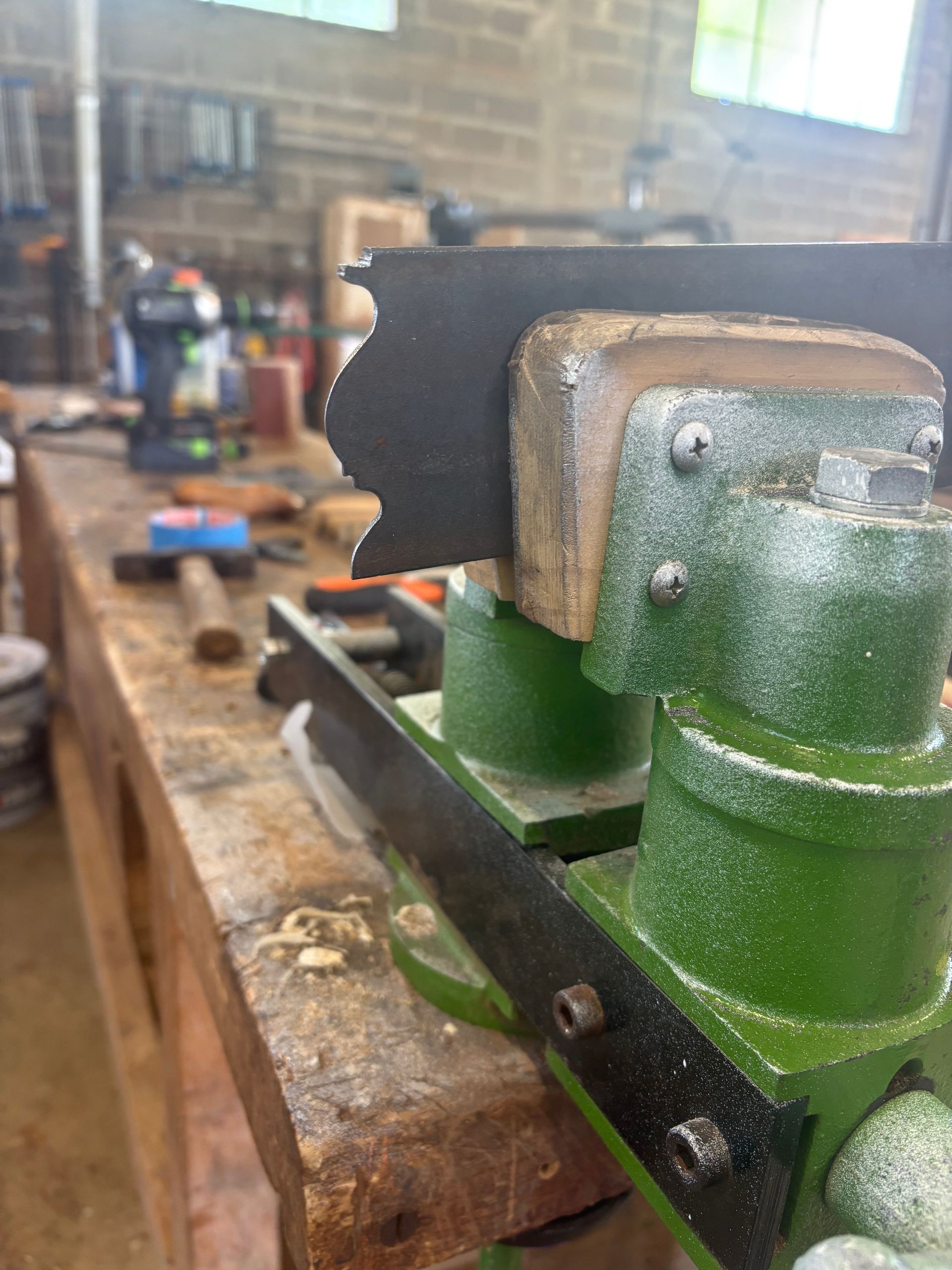 Étau vert fixé à un établi en bois dans un atelier, avec une mâchoire en métal noir.