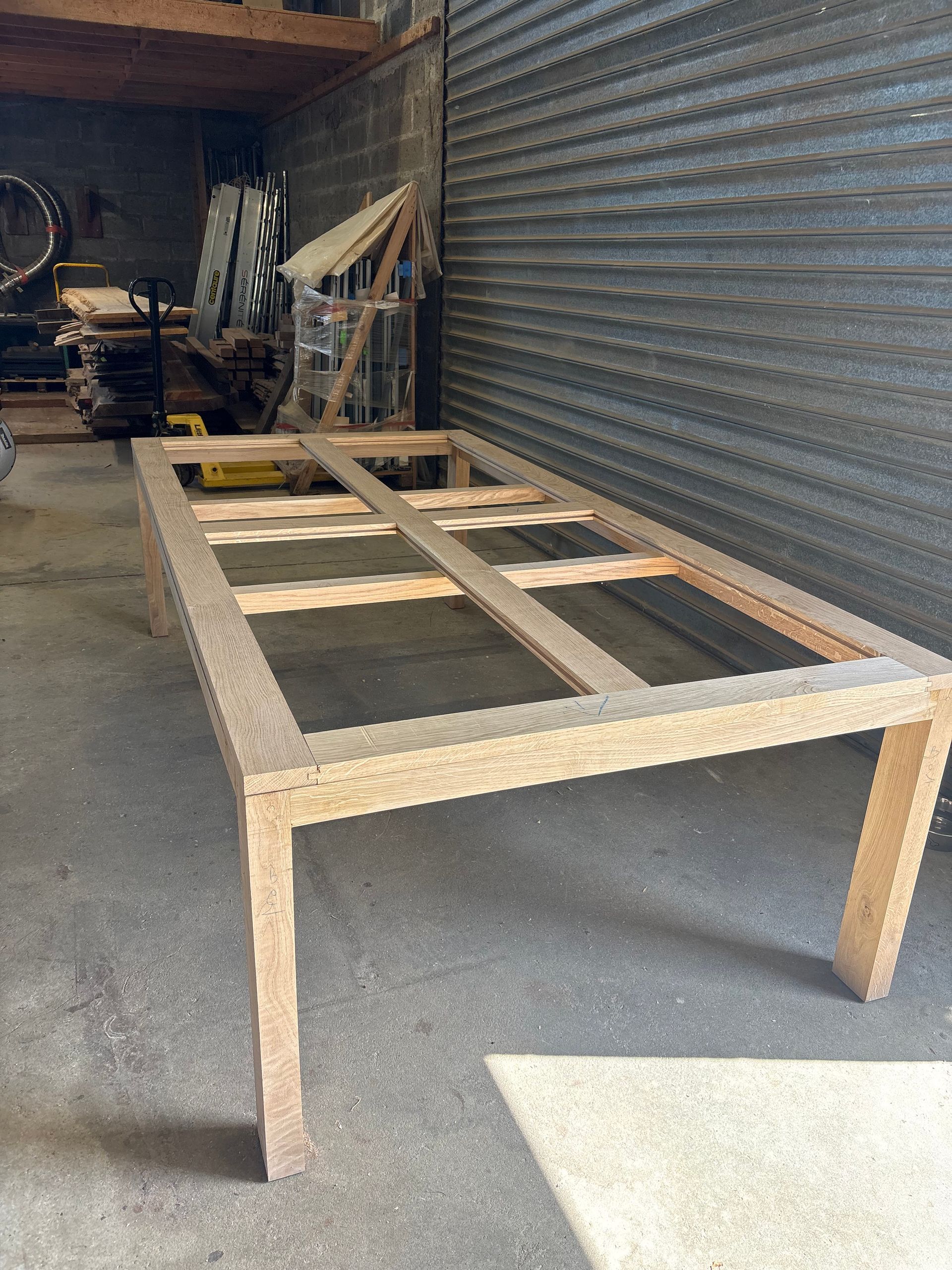 Table à structure en bois en cours de fabrication dans un atelier, à côté d’une porte métallique à enroulement.