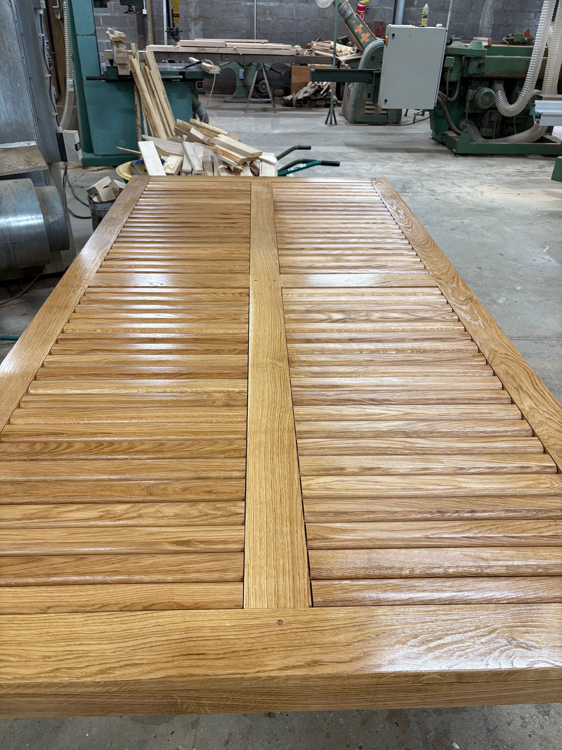 Table à lattes en bois dans un atelier, avec des machines industrielles en arrière-plan.