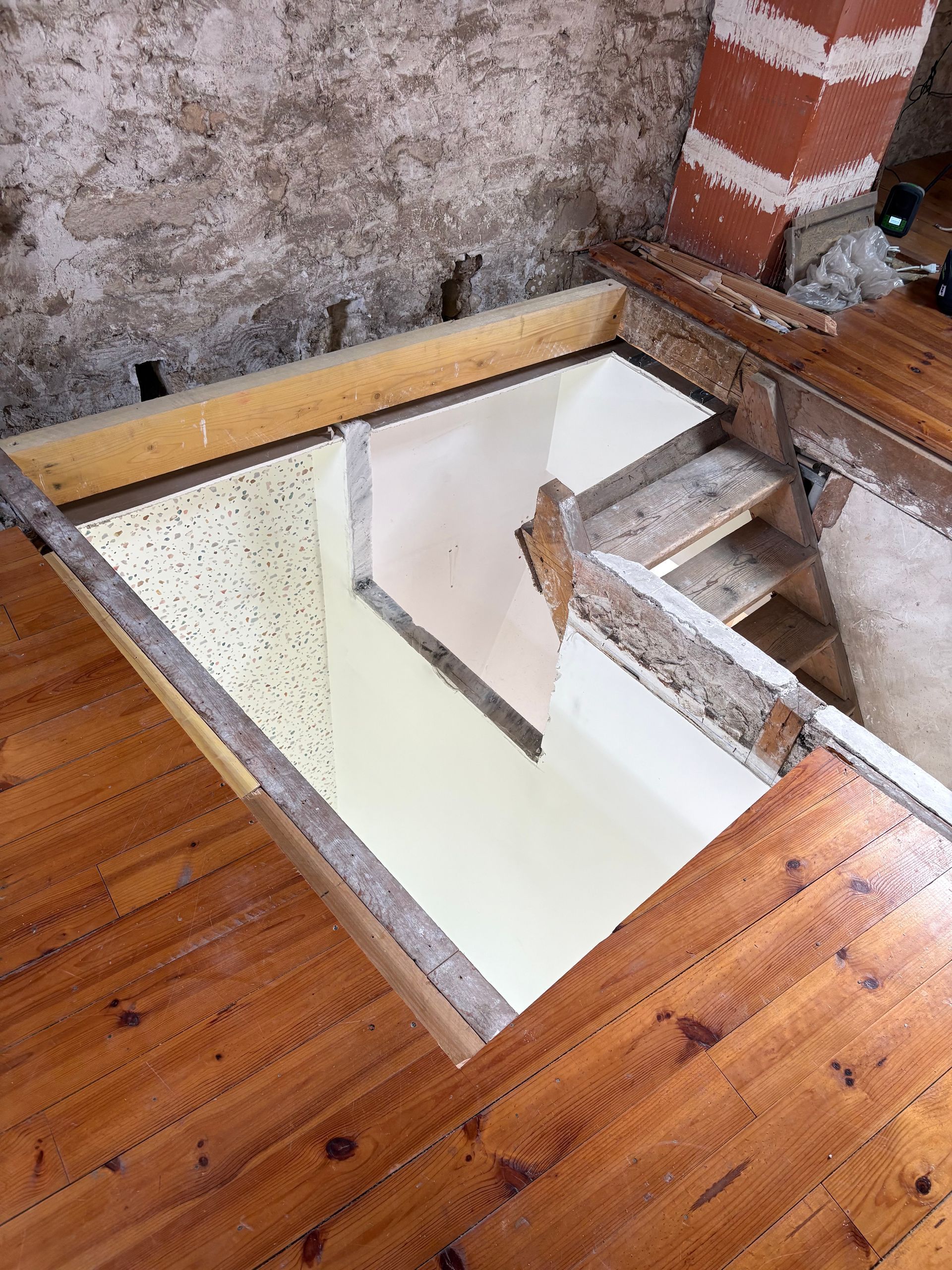 Trappe de plancher ouverte avec une échelle donnant accès à un niveau inférieur dans une pièce en bois.