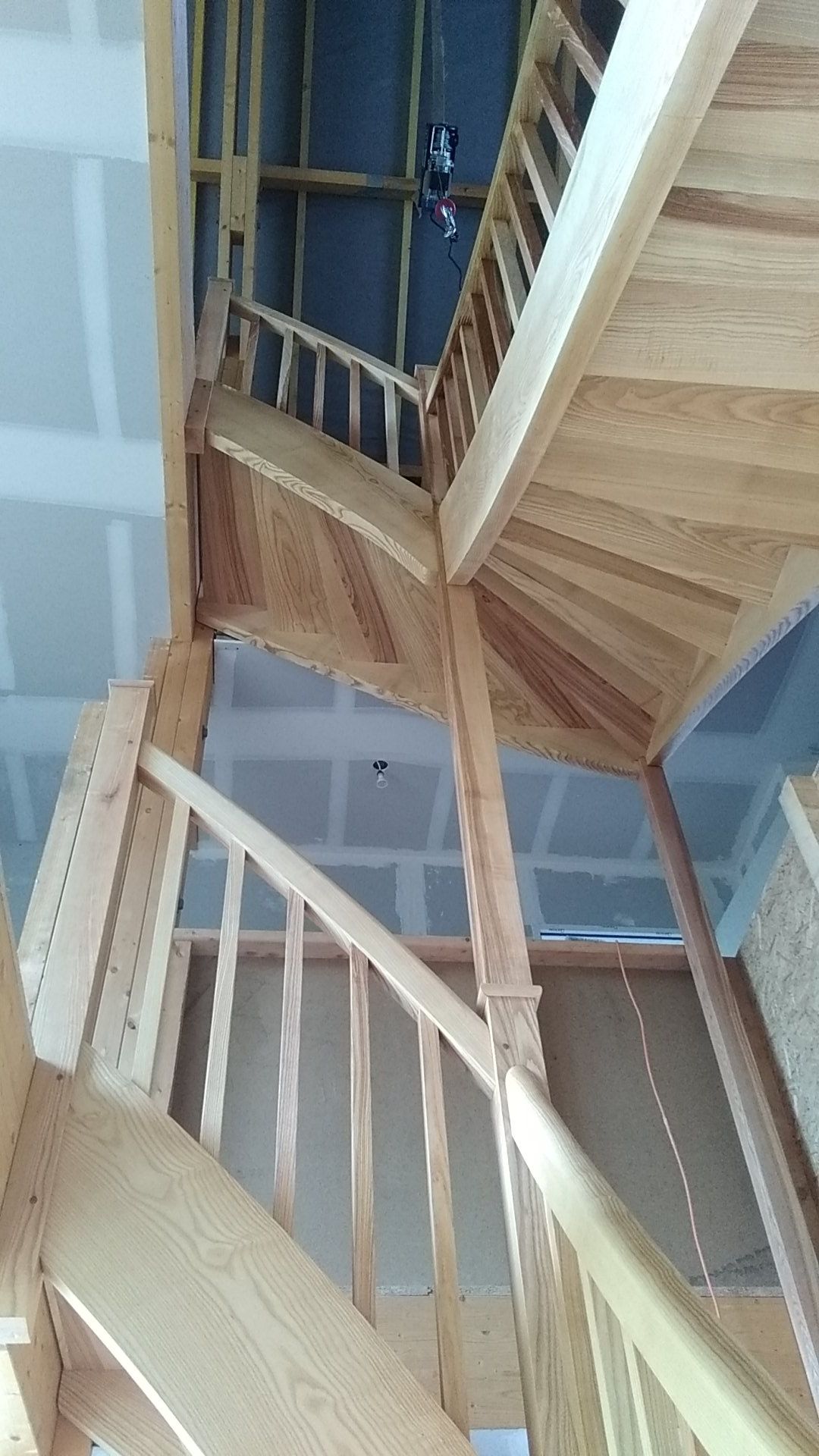 Escalier en bois avec des rampes claires, vu d’en bas dans un intérieur aux murs bleus.