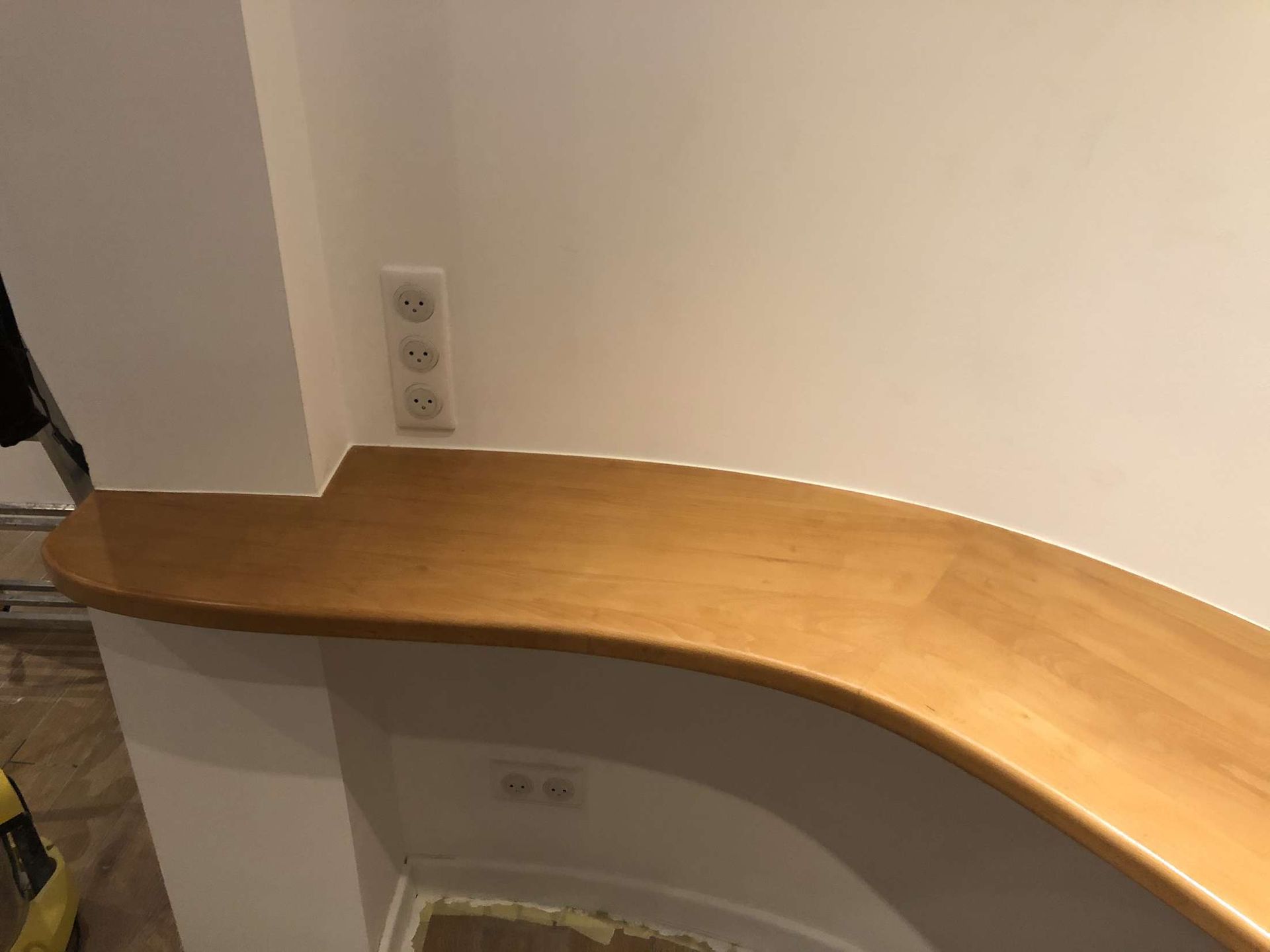 Comptoir de cuisine incurvé en bois contre un mur uni avec des prises électriques.