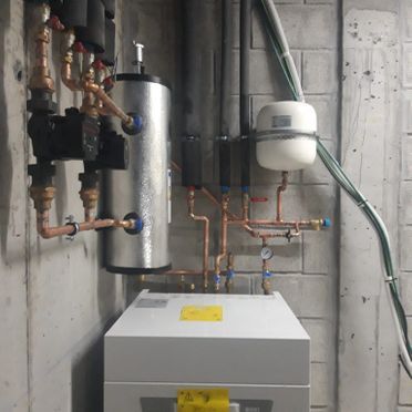 Una caldera con tubos de cobre conectados a ella está ubicada en una habitación.