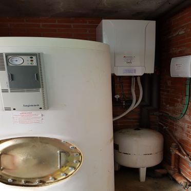 Un calentador de agua blanco está sentado al lado de una pared de ladrillos.