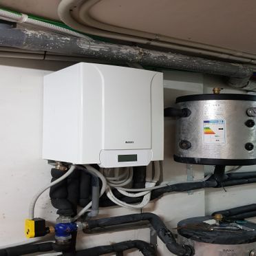 Una caldera blanca está colgada en una pared al lado de un tanque de acero inoxidable.