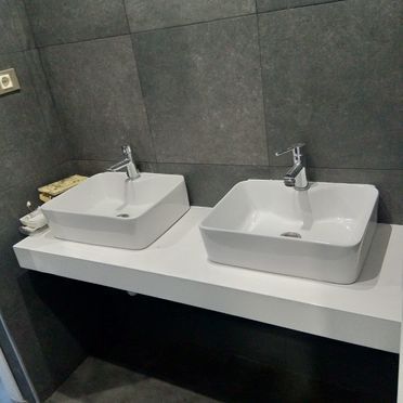 Hay dos lavabos cuadrados sobre una encimera blanca en un baño.