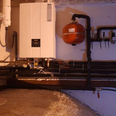 Una caldera blanca está colgada en una pared al lado de un tanque rojo.