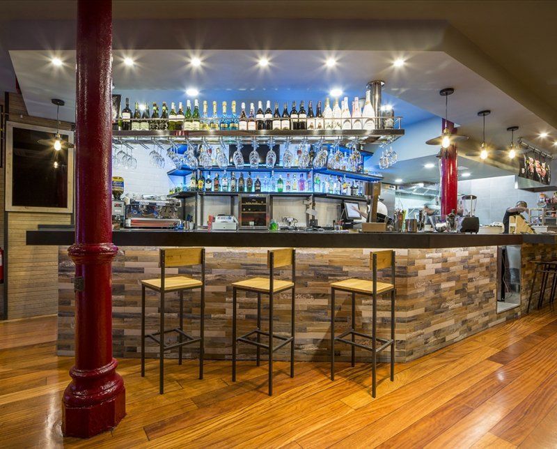 Un bar con taburetes y botellas de alcohol en los estantes.